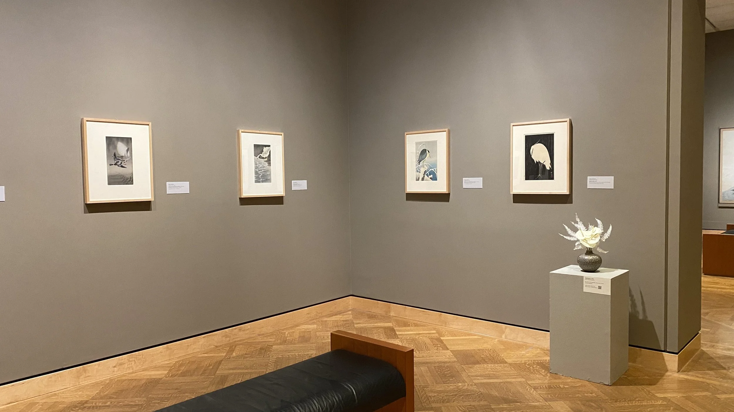 A white floral arrangement is placed on a pedestal within a gallery of Asian artworks