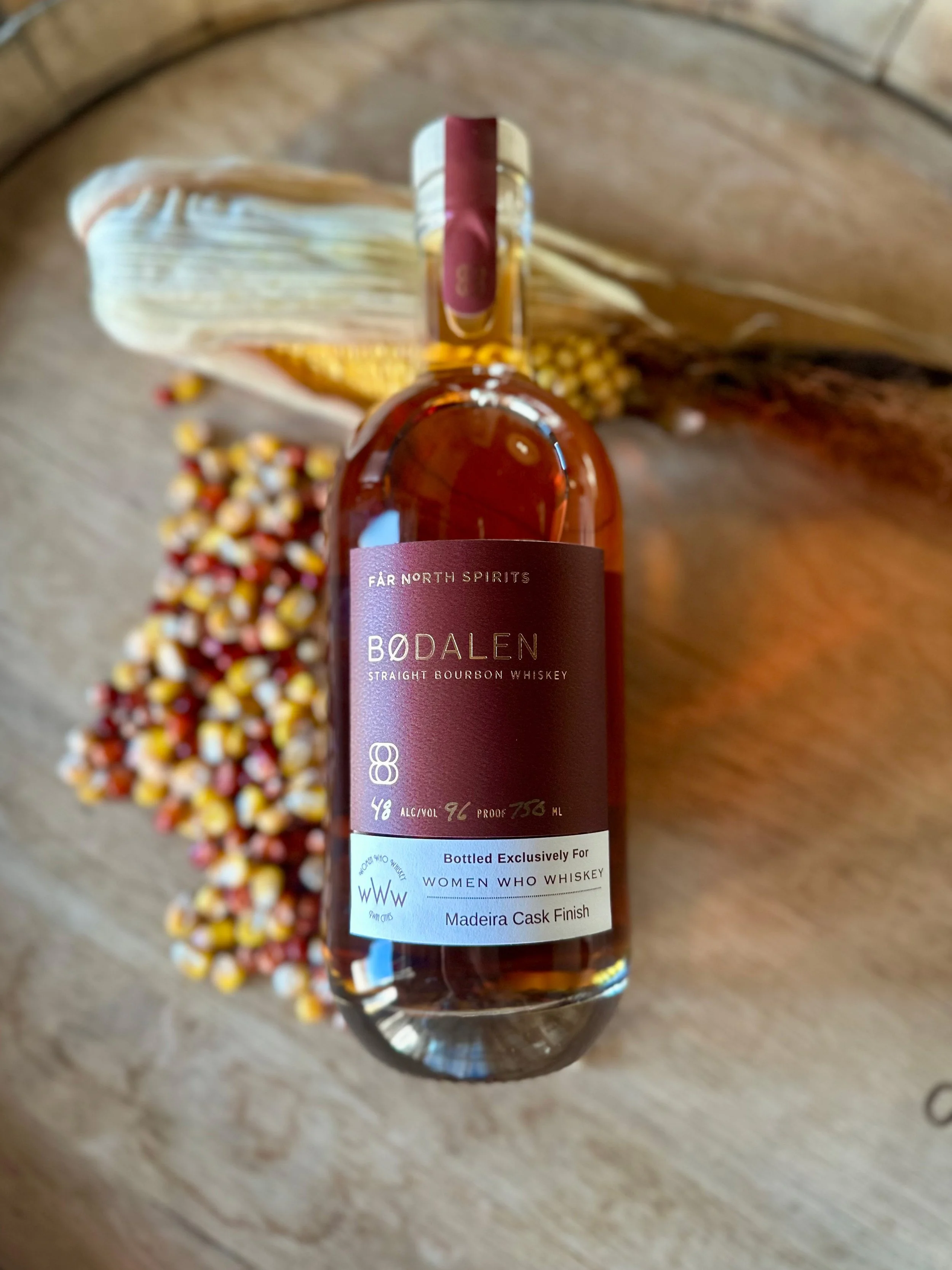 A bottle of Bødalen straight bourbon whiskey laying on a bed of corn kernels showing a label that indicates it is finished in Madeira casks, bottled exclusively for women who whiskey.