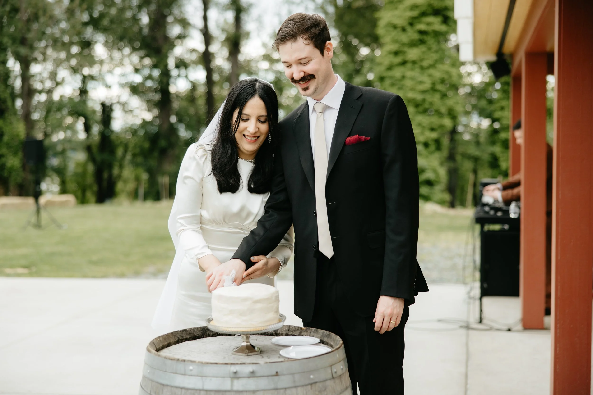 A bride and groom cutting a wedding cake outdoors.
