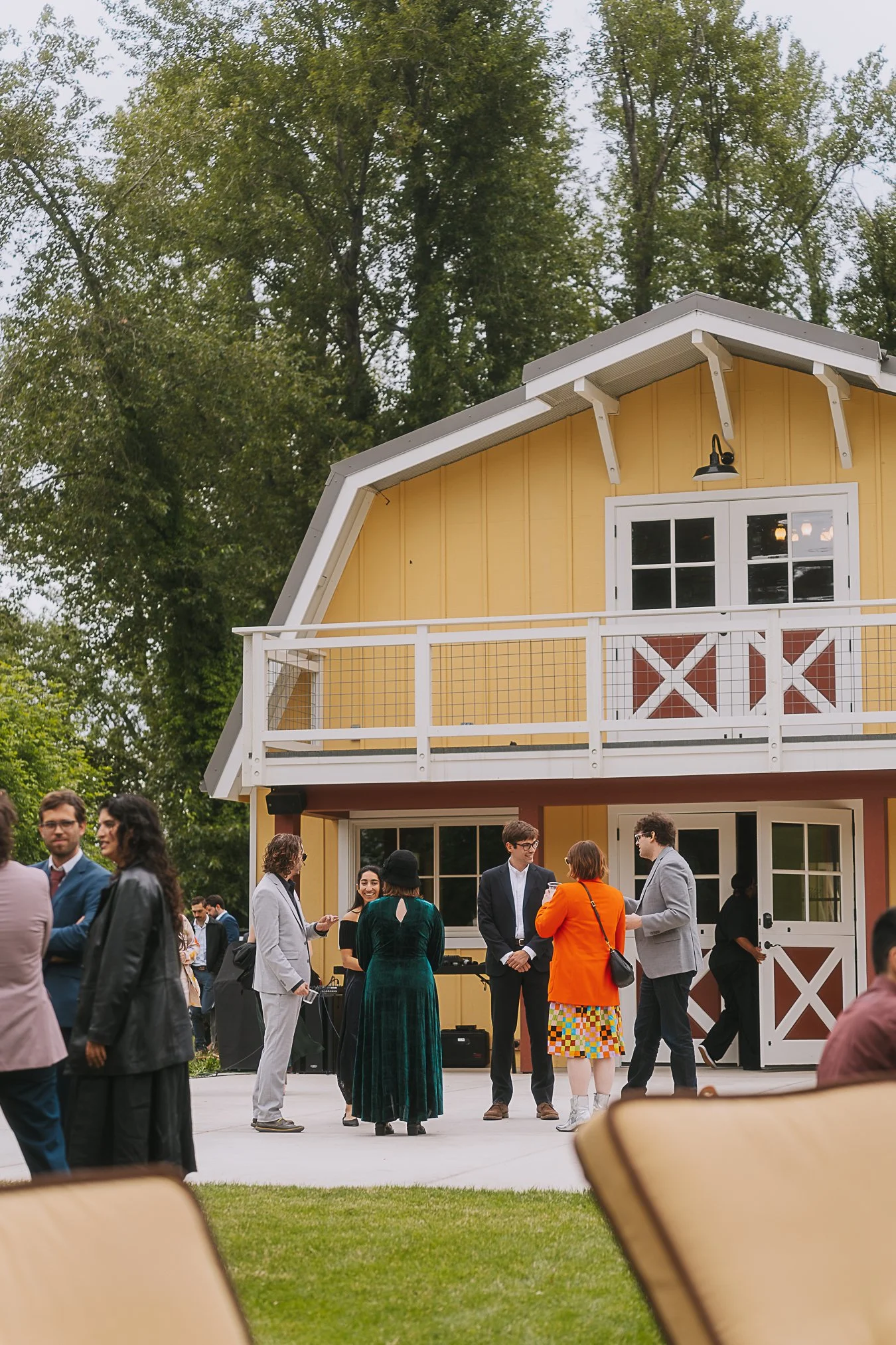 People socializing outside a yellow barn-style building during an event, with some engaged in conversations and others standing in groups.