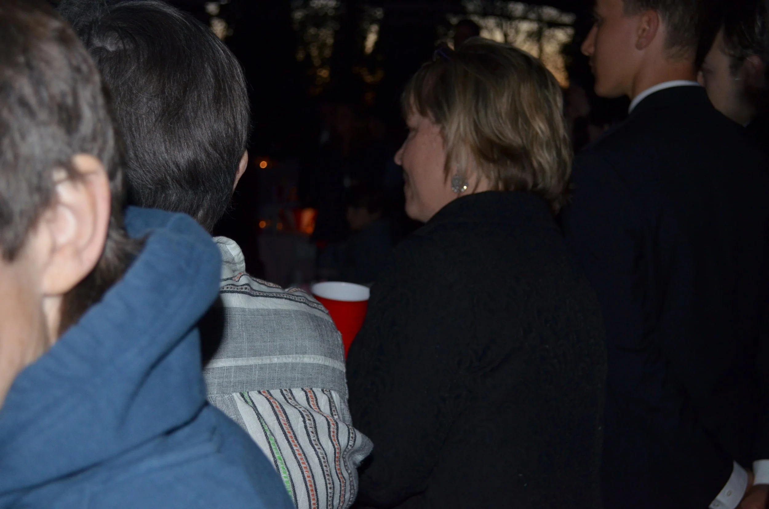 People gathered outdoors at night, some holding red cups, likely at a social event or party.