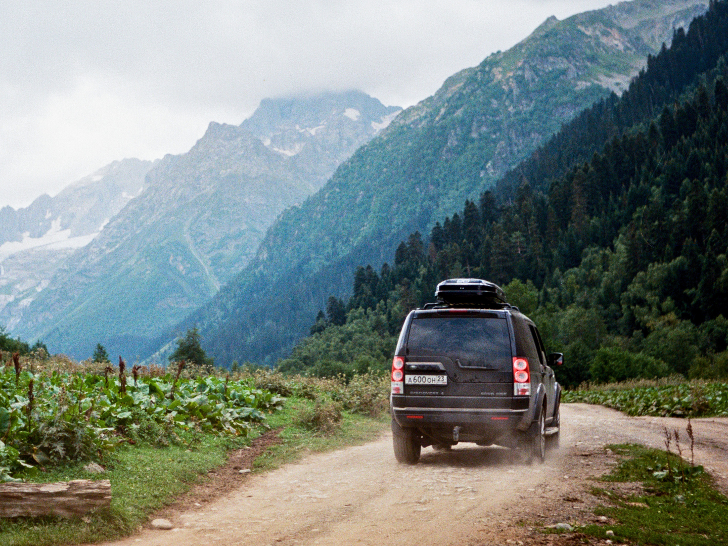 Black Mercedes-Benz GL450 driving on open road surrounded by green trees with a mountain in the background and a partly cloudy sky.