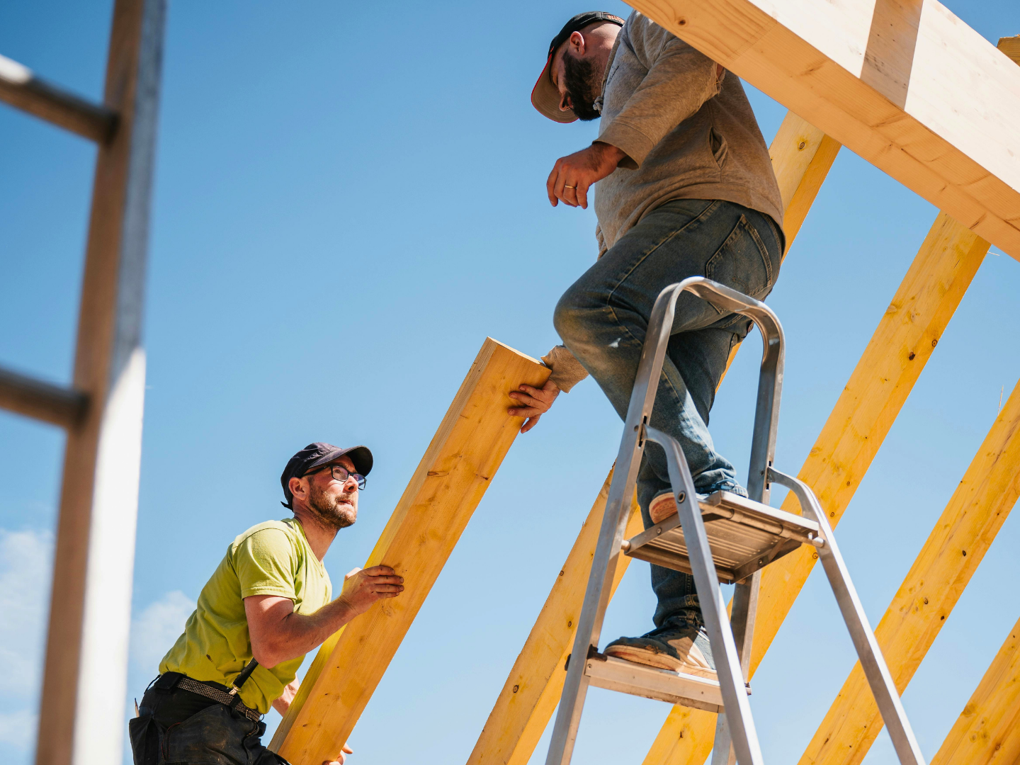 Three construction workers wearing white helmets and yellow safety vests inspecting a cinder block wall at a construction site.
