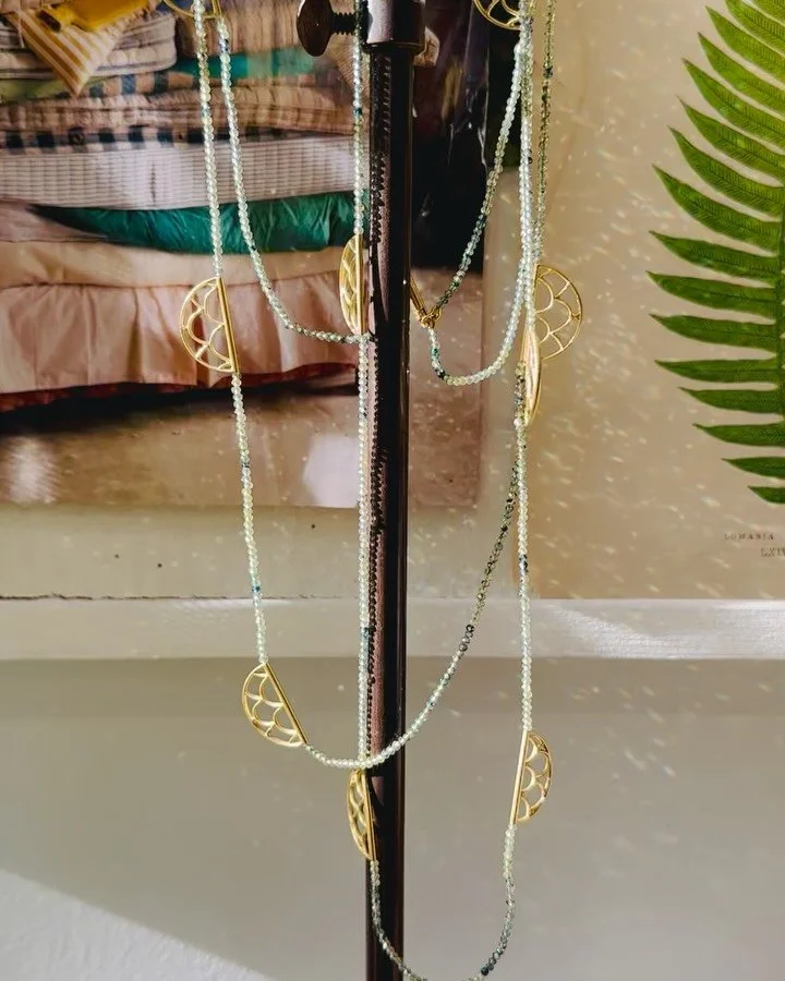 Light and dark, always shifting.
.
The Interlace Necklace comes to life in movement. Faceted green sapphires catch the sunlight with a quiet sparkle, while each patterned crescent bead casts its own soft shadow. In dappled shade, the necklace becomes