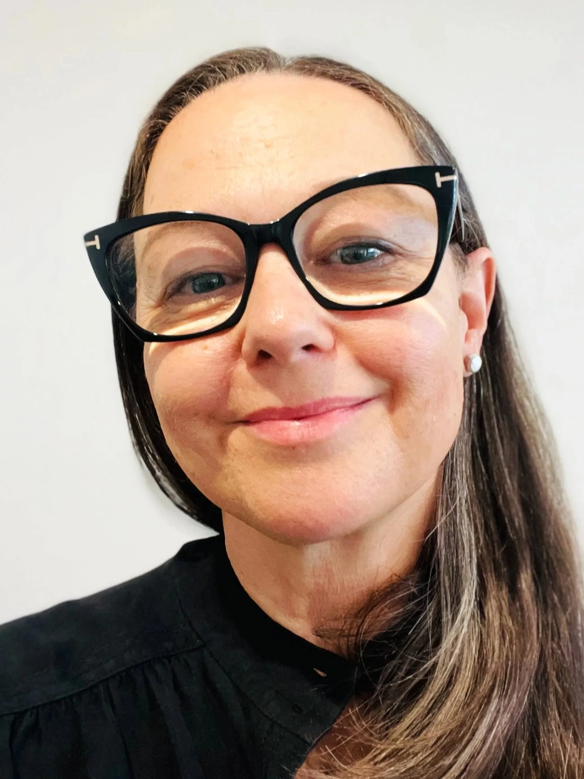 a smiling woman with black glasses and long salt and pepper hair hair