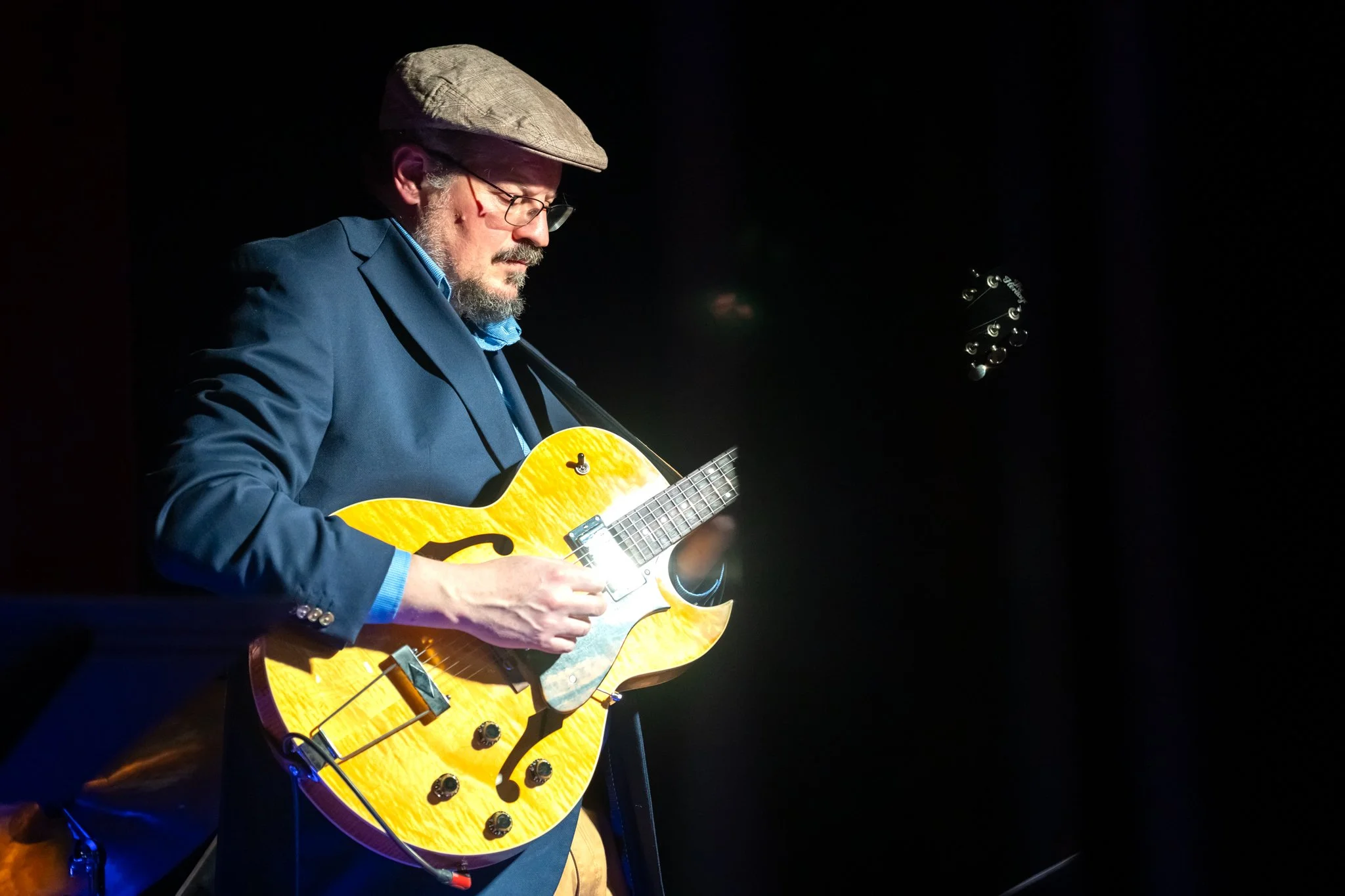 Man in hat playing electric hollowbody guitar onstage