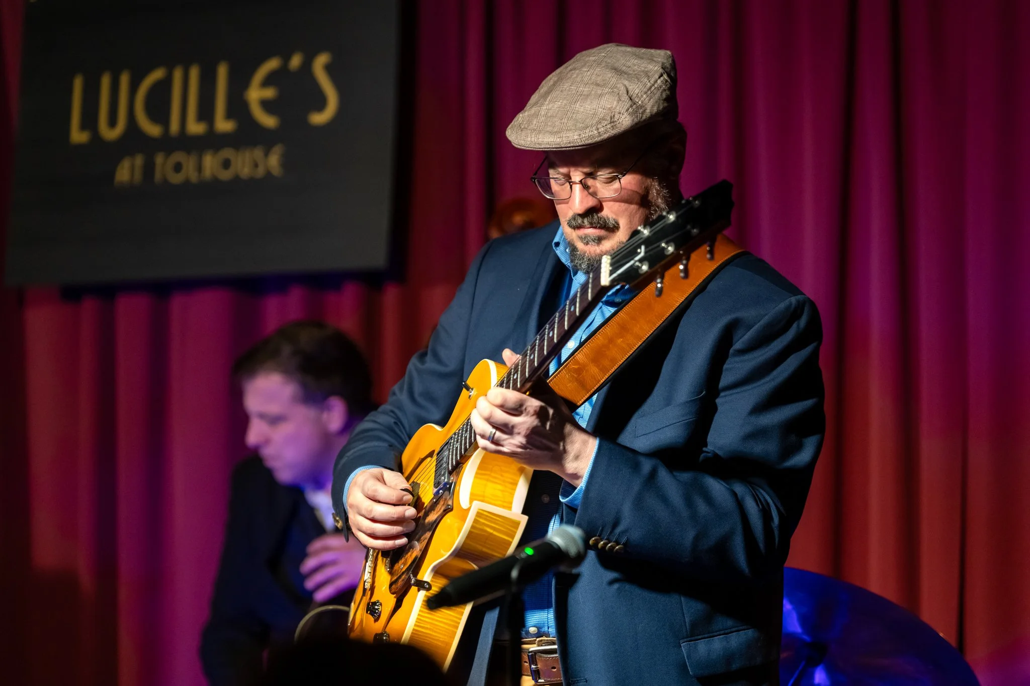 Man in hat playing electric hollowbody guitar onstage in front of man playing upright bass.