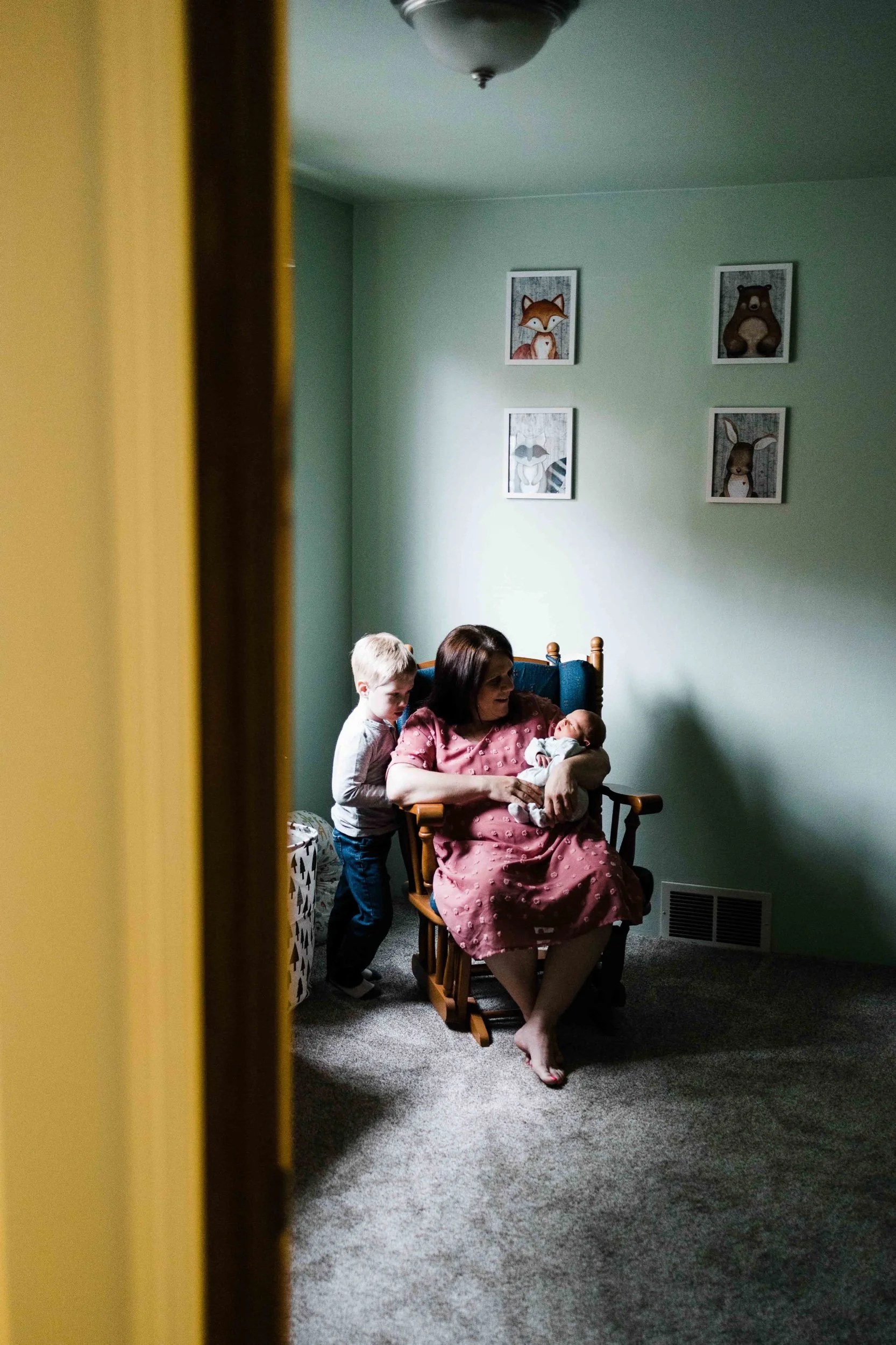 Mother and big brother hold newborn baby brother in the nursery of their Seattle home.