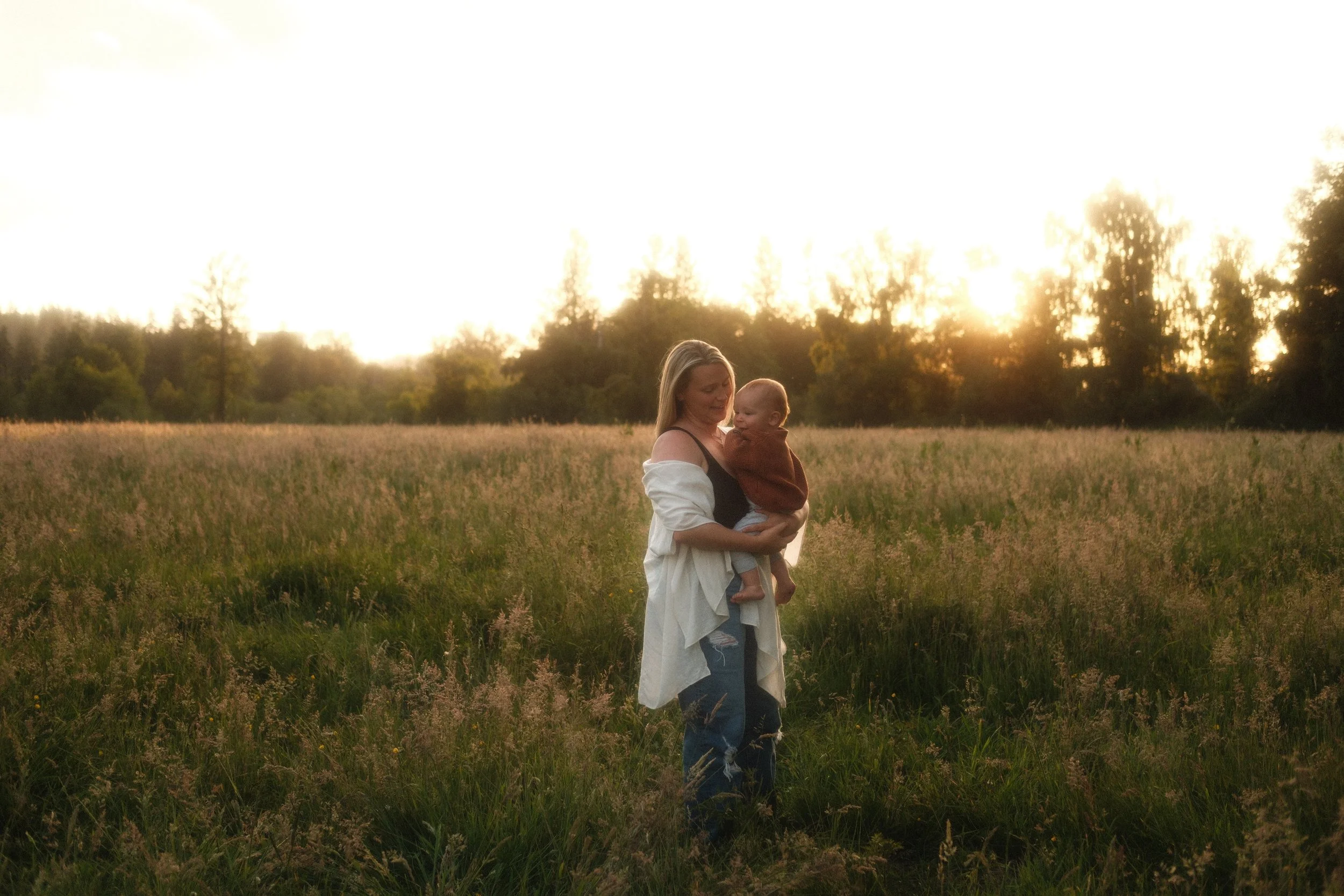Mother holding her baby in a grassy Seattle field at golden hour, relaxed family photography session.