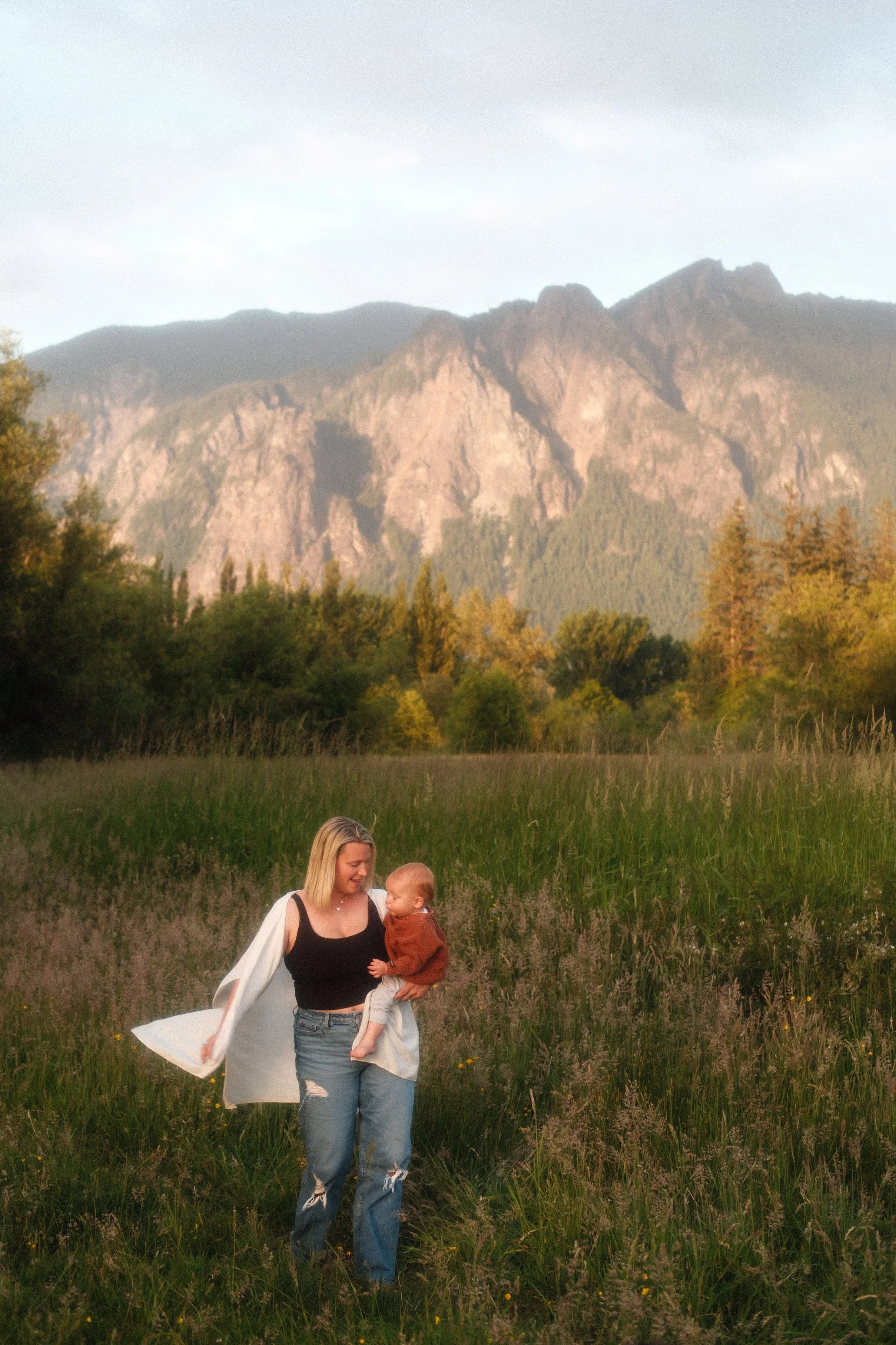 Mother carrying her baby with Mount Si in the background, outdoor Seattle family photography in North Bend.