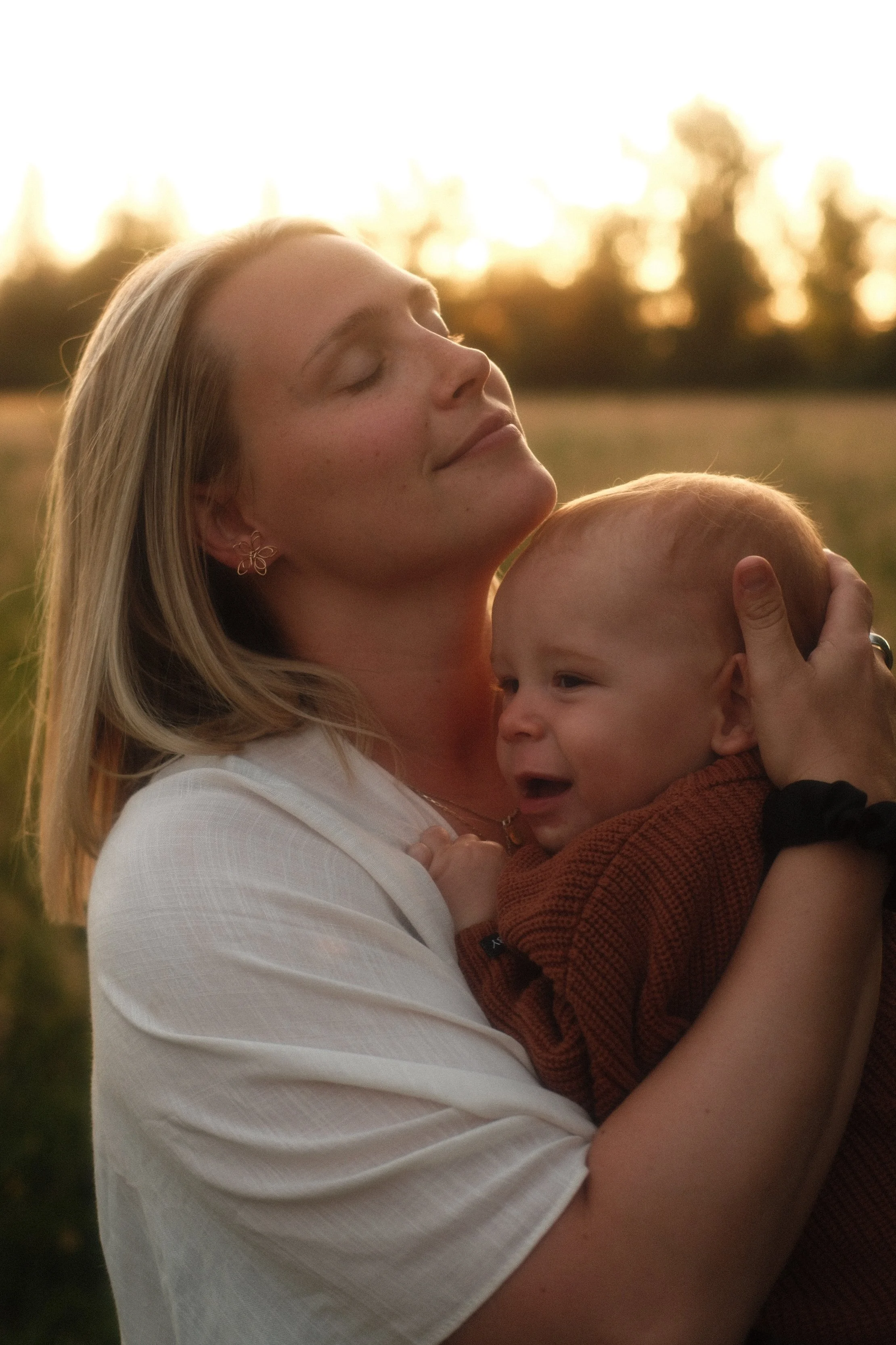 Tender moment of a mother holding her baby close at sunset, photographed during a Seattle motherhood session.