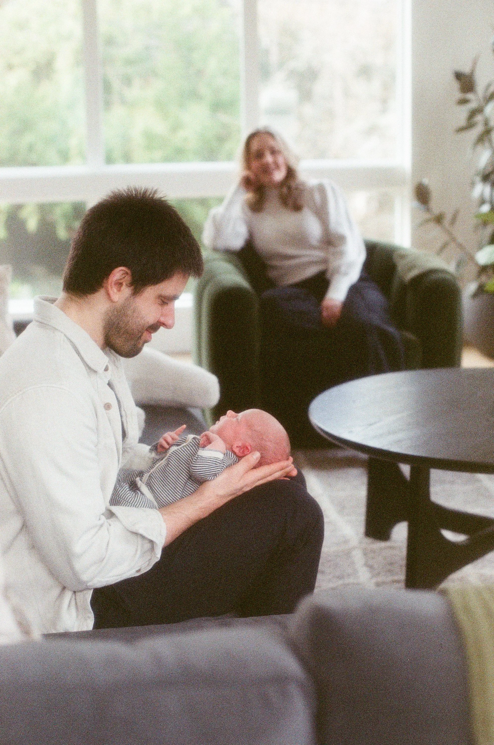 Seattle father of a newborn holds his baby boy as mom watches him lovingly. 
