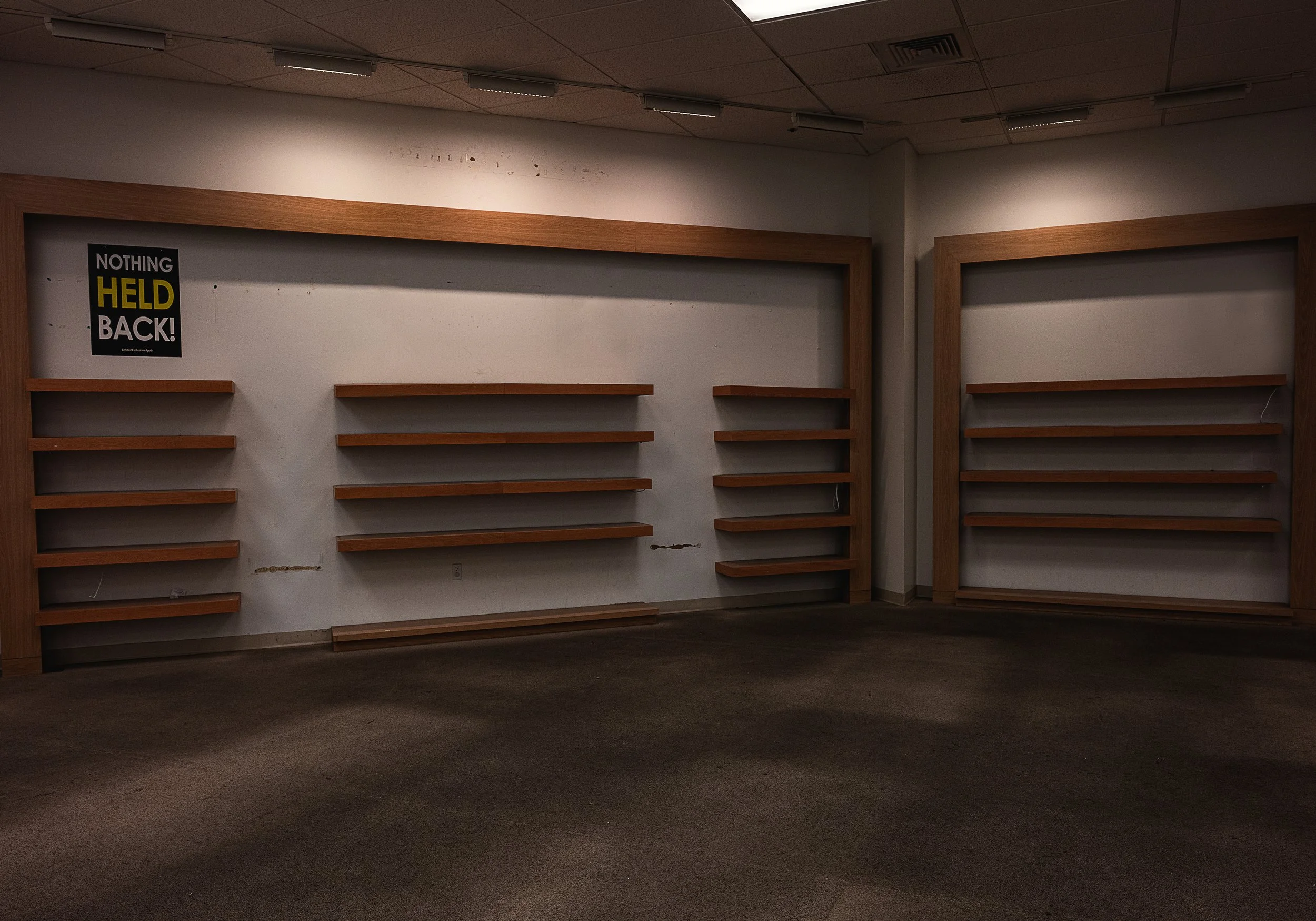 Empty office space with wooden shelves on the wall and a poster that says 'Nothing Held Back!'