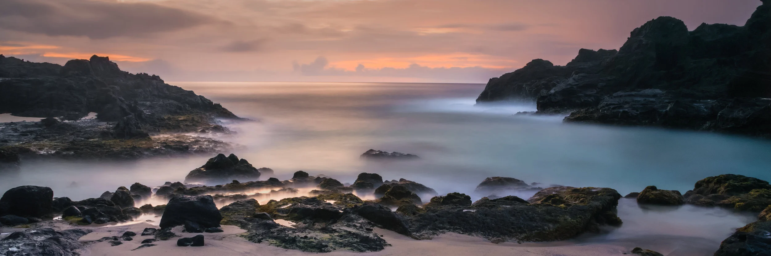Eternity Beach is a fine art photograph of Halona Beach Cove on the island of Oahu, Hawaii by Jason Matias. It is a panoramic, long exposure with oranges, salmons, pinks, blues and lava rock. 