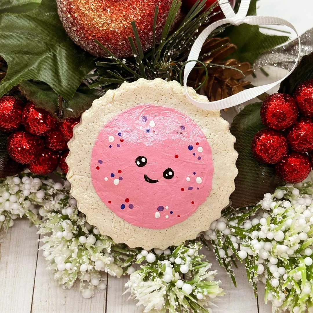 Round Christmas cookie ornament with a pink center and smiling face.