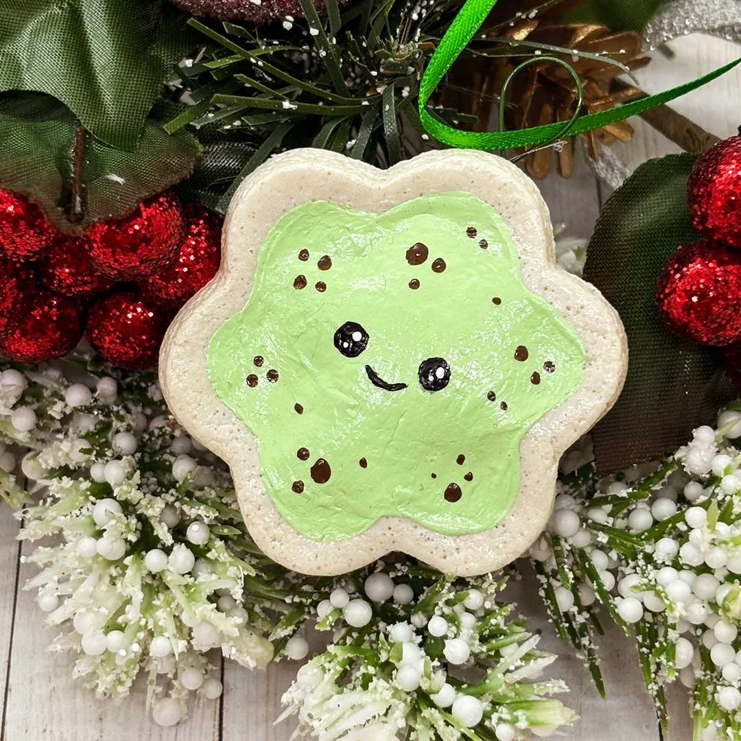 Smiling flower shaped cookie with painted mint frosting and sprinkles.