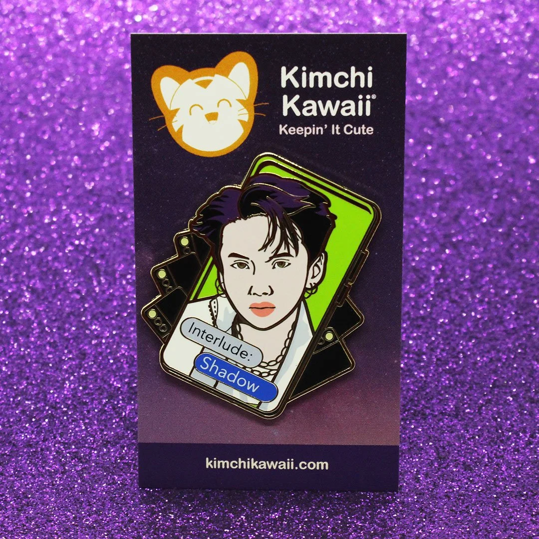Enamel pin of Suga from BTS popping out of a smart phone screen with other smart phones behind him.