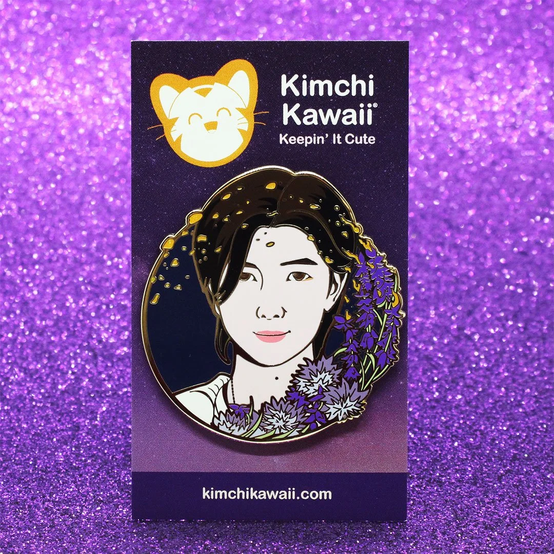 Enamel pin of RM from BTS surrounded by purple flowers and orange sparks.