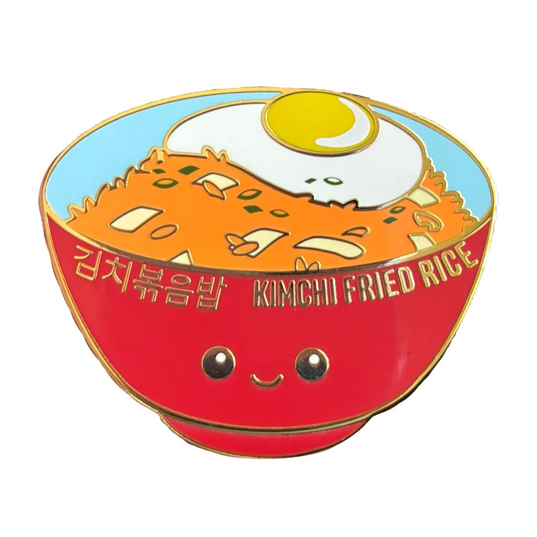 Enamel pin of kimchi fried rice in a red bowl with a smiling face.
