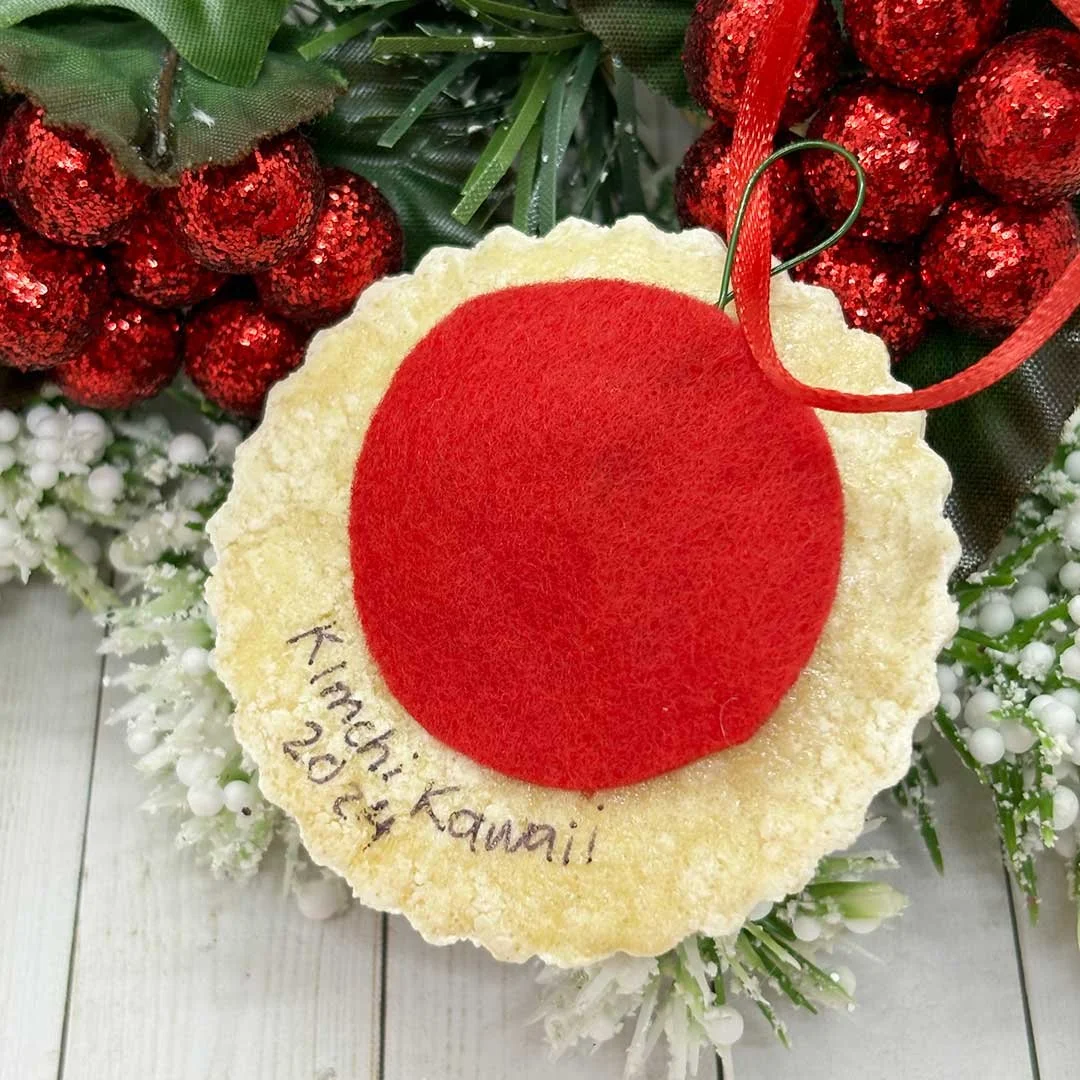 Back of a round Christmas cookie ornament with felt backing and a signature that says 'Kimchi Kawaii, 2024'.