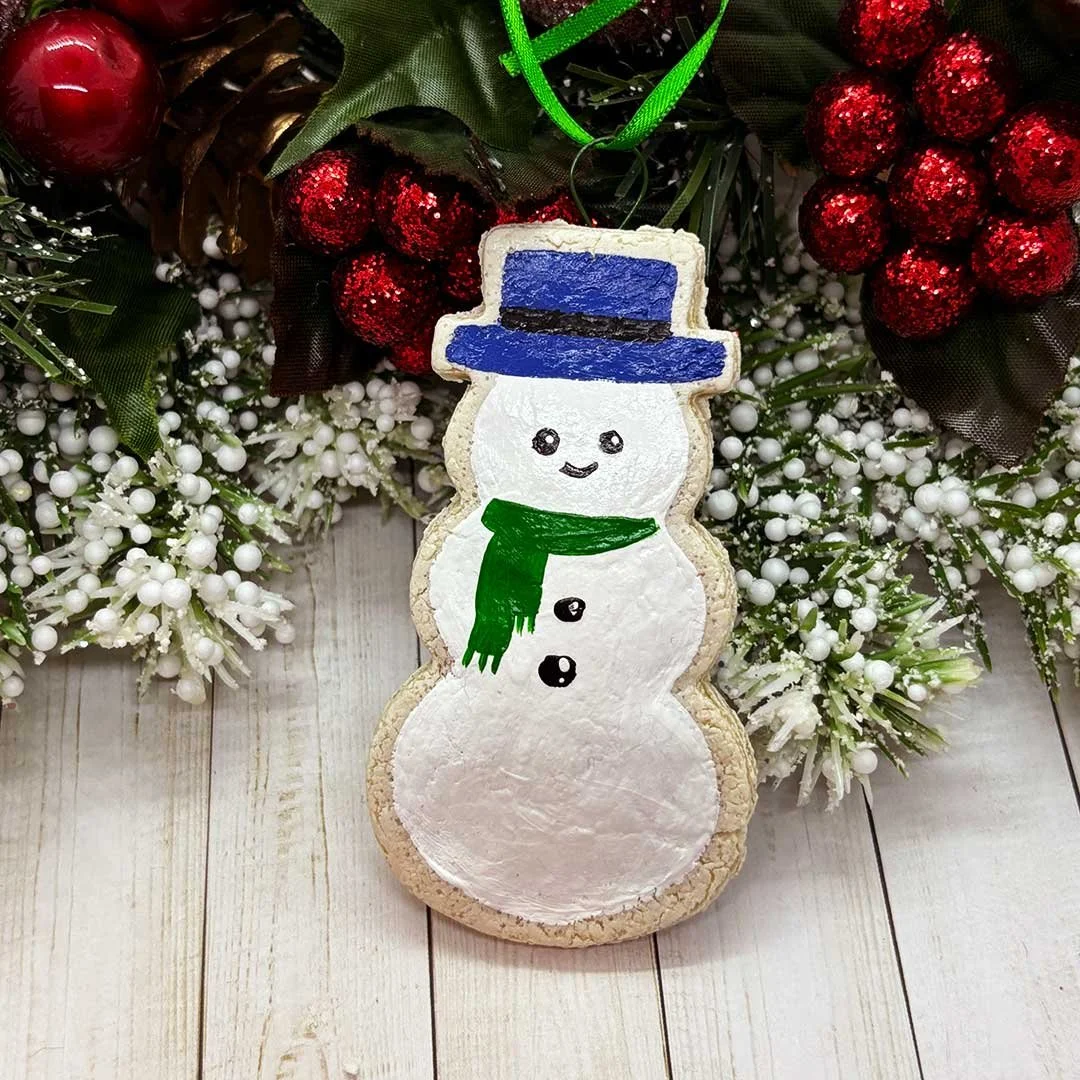 Cookie ornament of a snowman with a blue hat and green scarf.