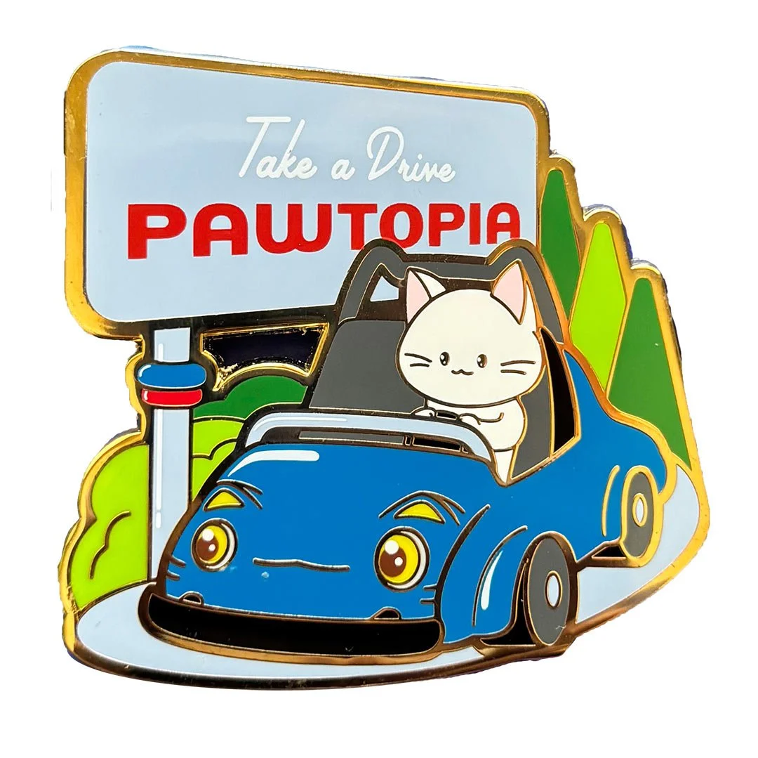 Enamel pin of a cat driving a blue car with a sign that says 'Take a drive. Pawtopia'.
