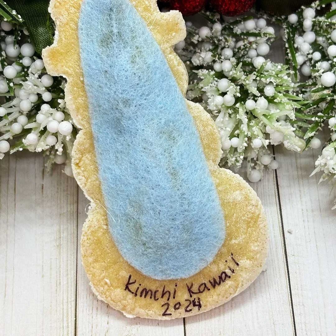 Back of a snowman cookie ornament with blue felt and 'Kimchi Kawaii, 2024'.