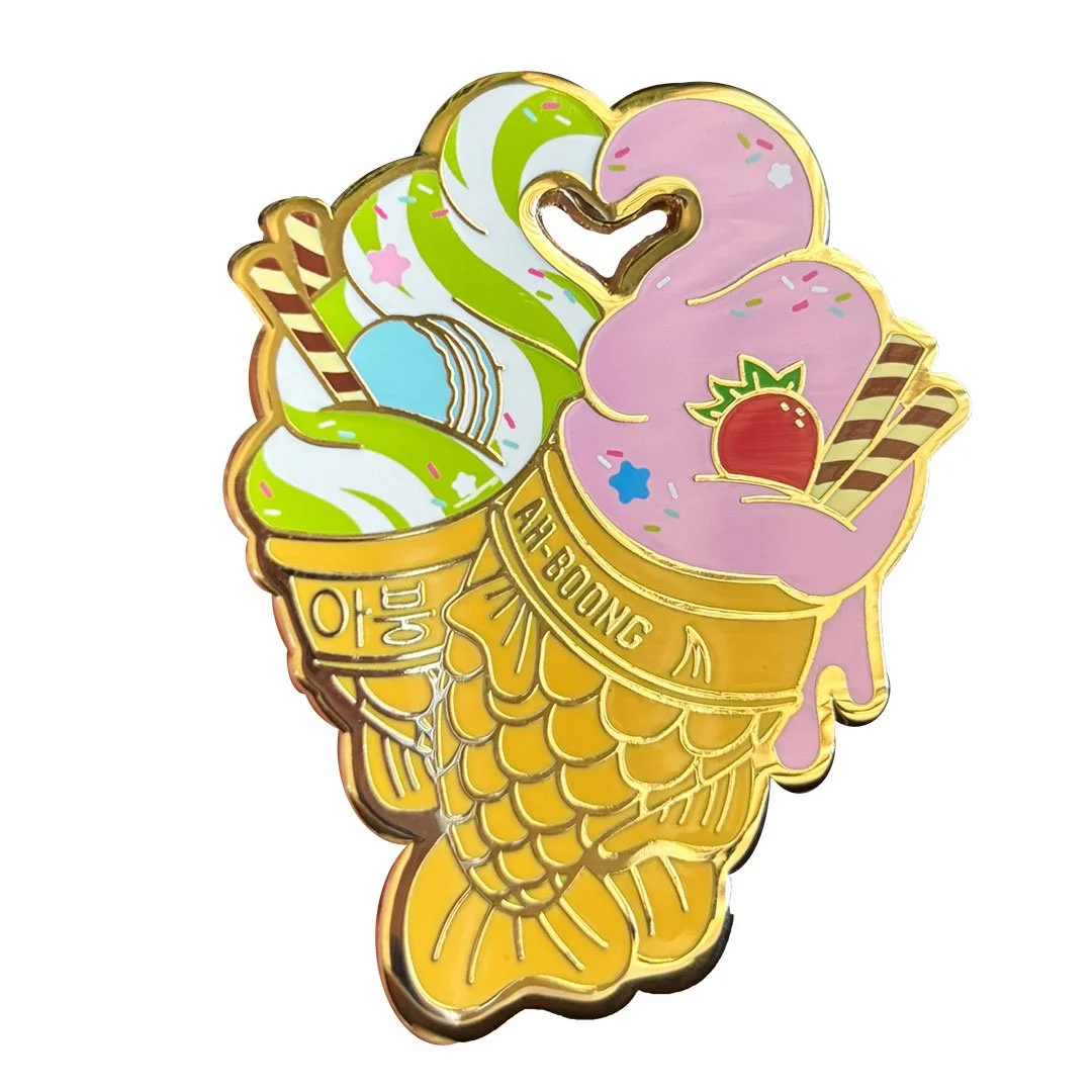 Enamel pin of two fish shaped cones with soft serve ice cream.