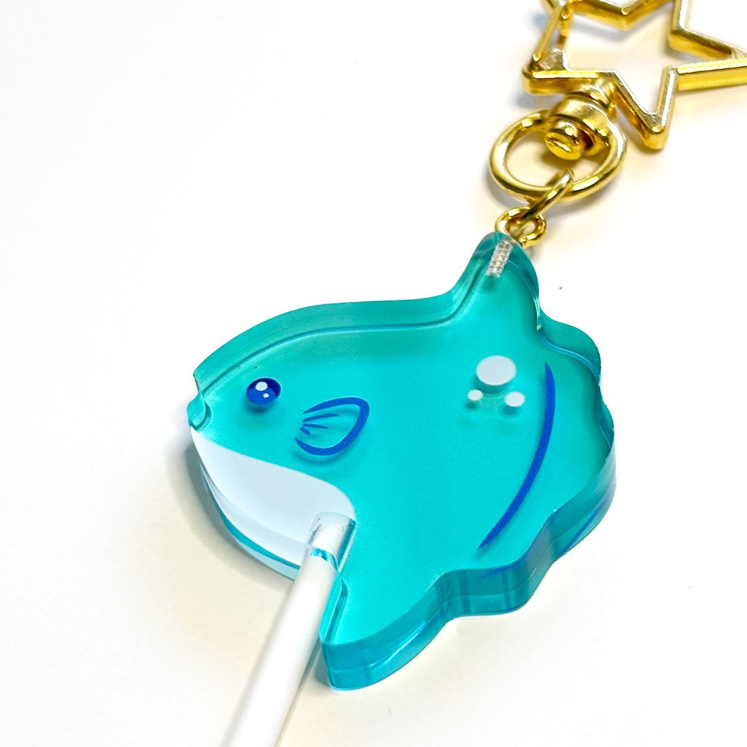 Detail of a blue acrylic mola mola lollipop charm with a gold clasp.