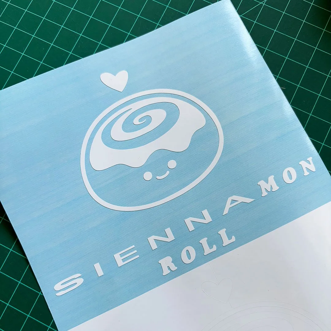 White vinyl sticker of a cute cinnamon roll with the words 'Siennamon Roll' below.