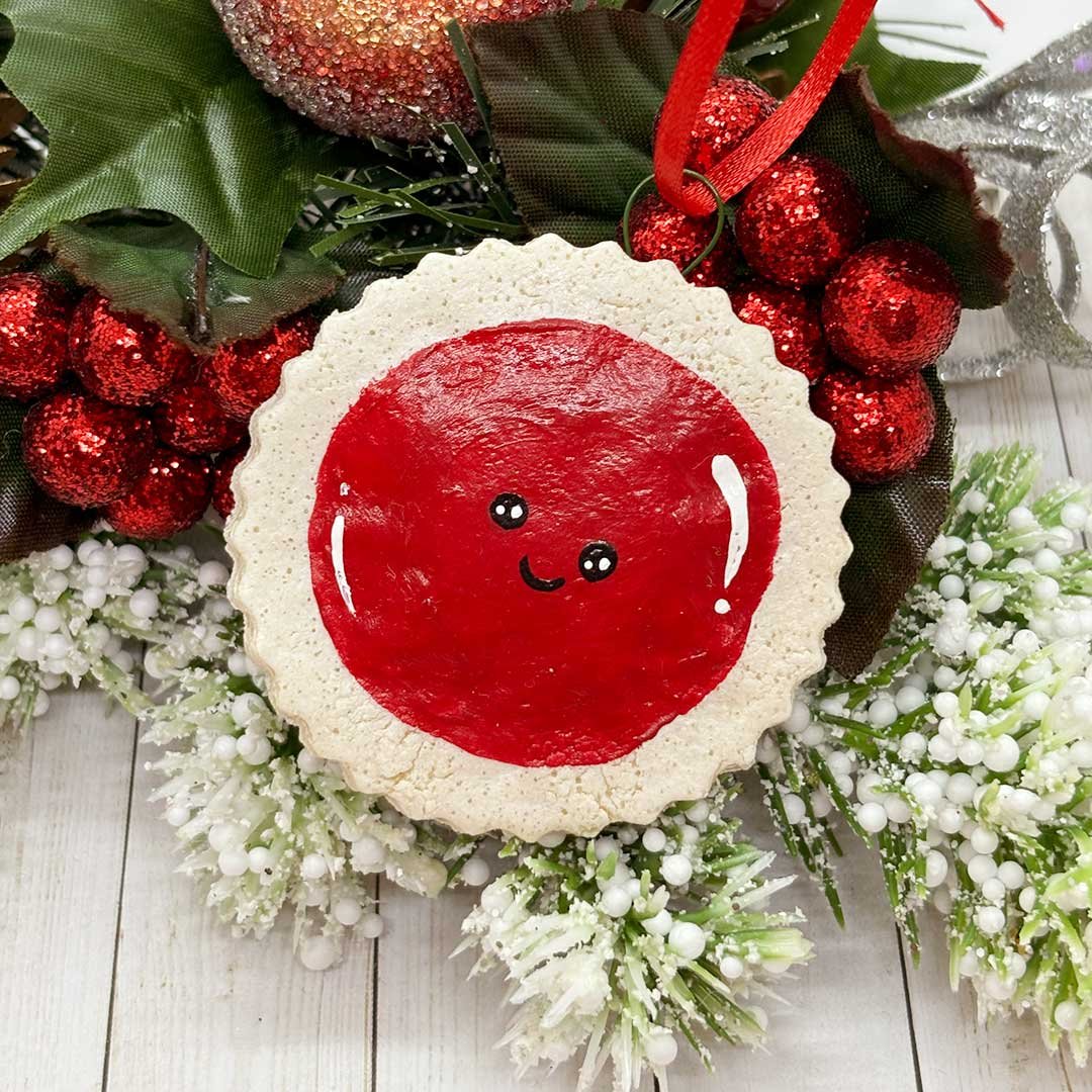 Round Christmas cookie ornament with a red center and smiling face.