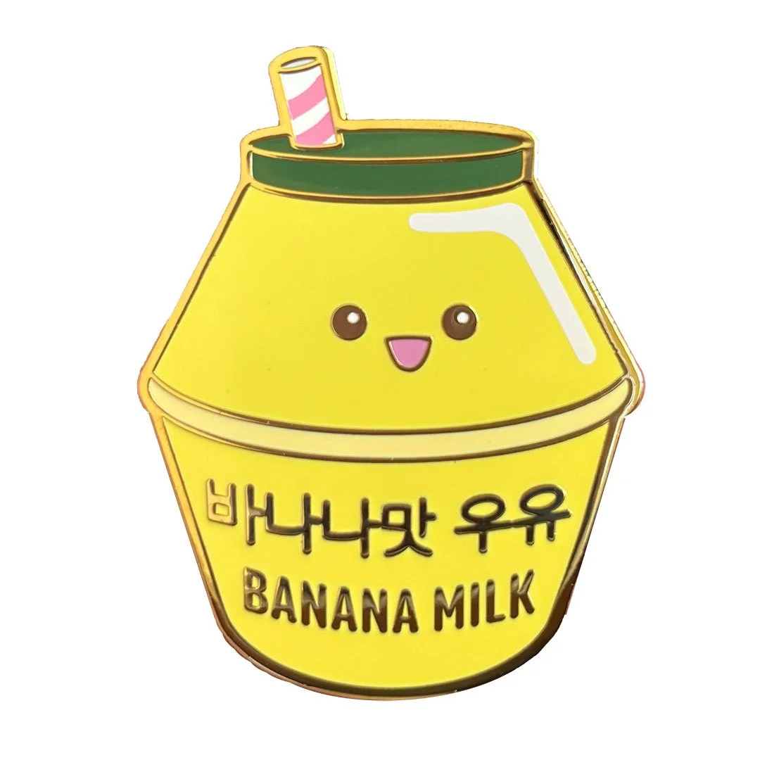 Cute enamel pin of a yellow banana milk bottle with a green lid and small straw.