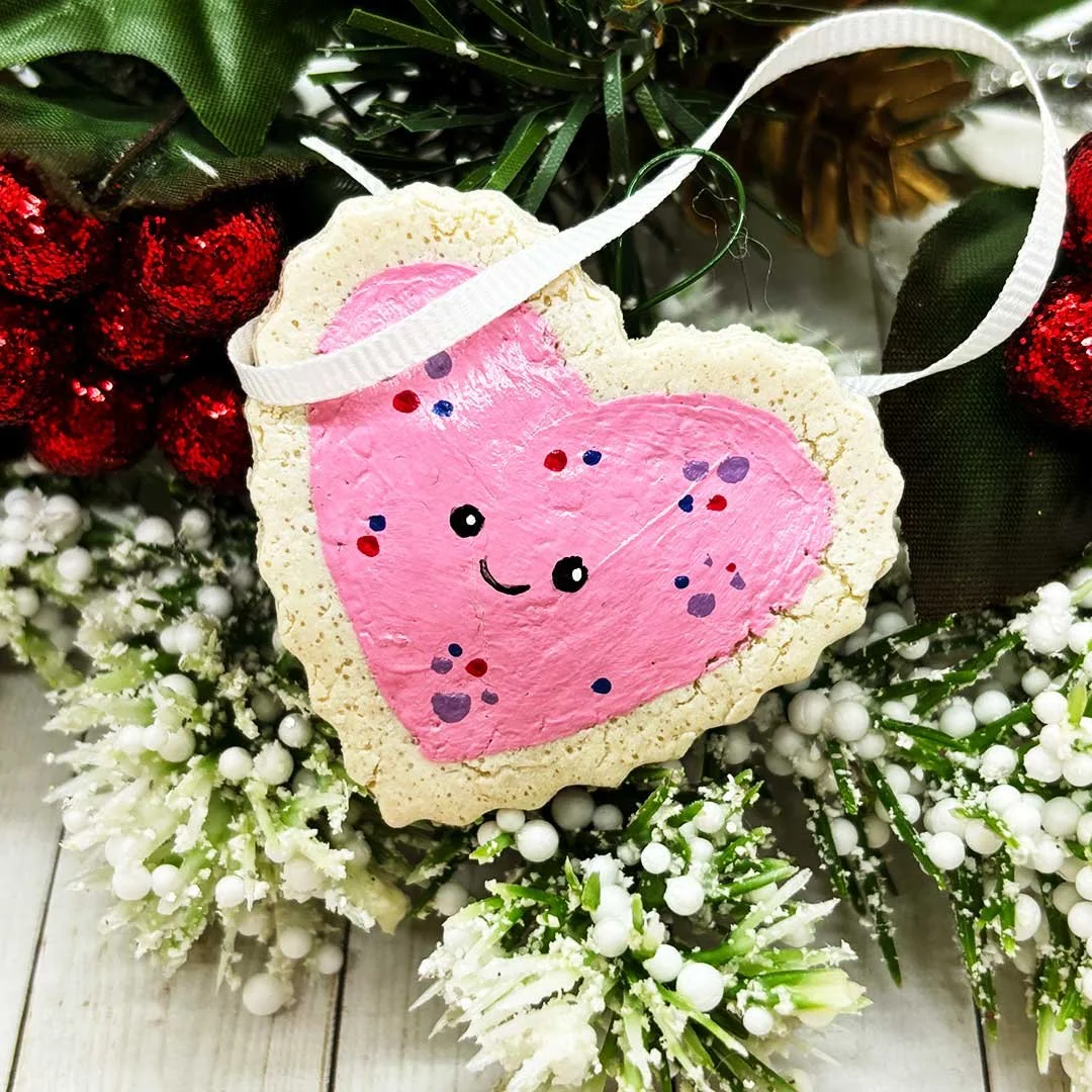 Smiling heart ornament with painted pink frosting and sprinkles.