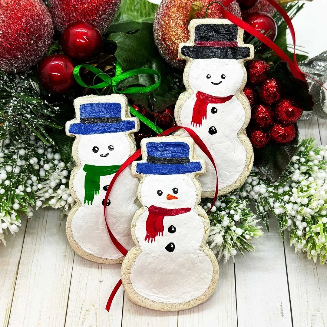 Three cookie ornaments shaped like snowmen with painted on hats and scarves.