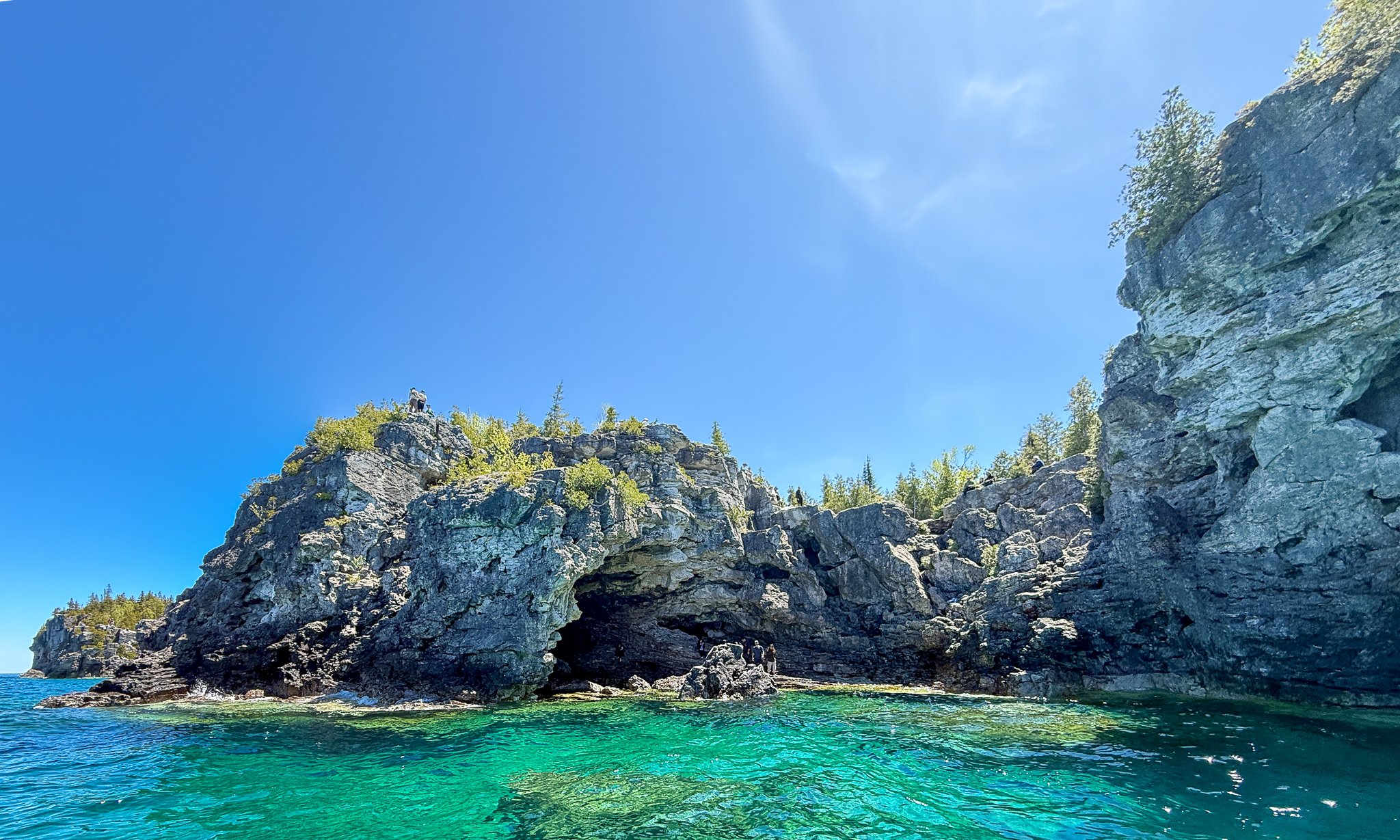 View from Georgian Bay looking toward the Grotto on the Bruce Peninsula, showing cliffs, bright blue sky, and clear turquoise water.