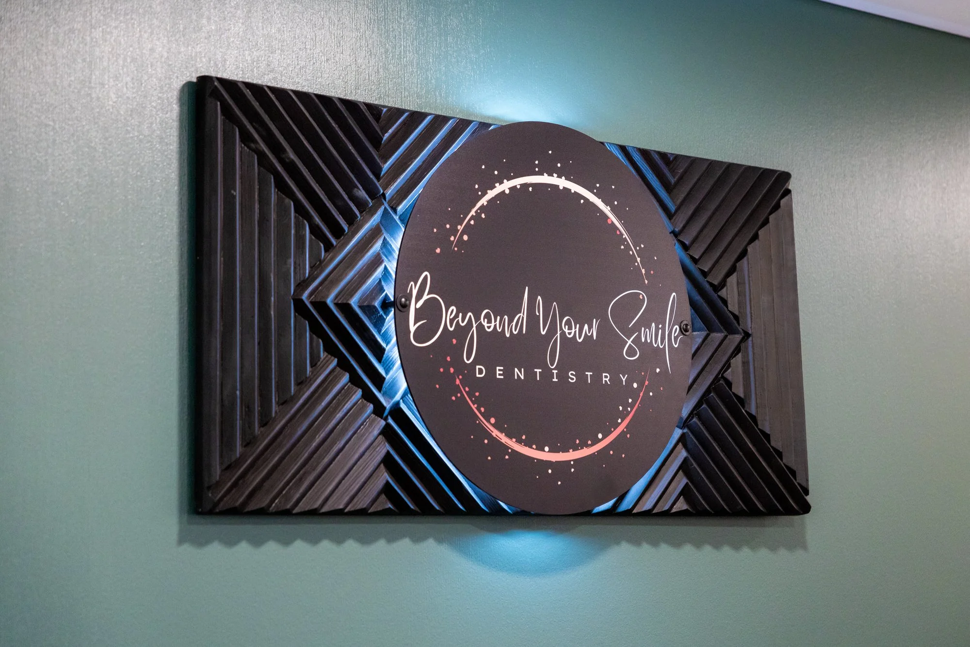Signboard for Beyond Your Smile Dentistry with a decorative black frame and a dark circular background with white and pink accents.