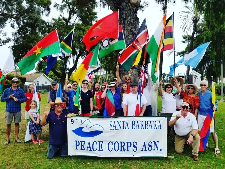 Photo: After marching in the 2019 July 4th parade, Santa Barbara are Returned Peace Corps Volunteers holding the colorful flags of the countries in which they served, standing behind the Santa Barbara Peace Corps Association banner.