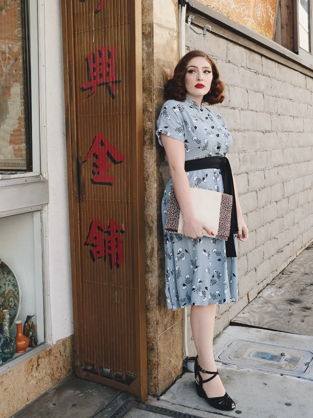Woman in vintage blue dress standing by Chinatown storefront