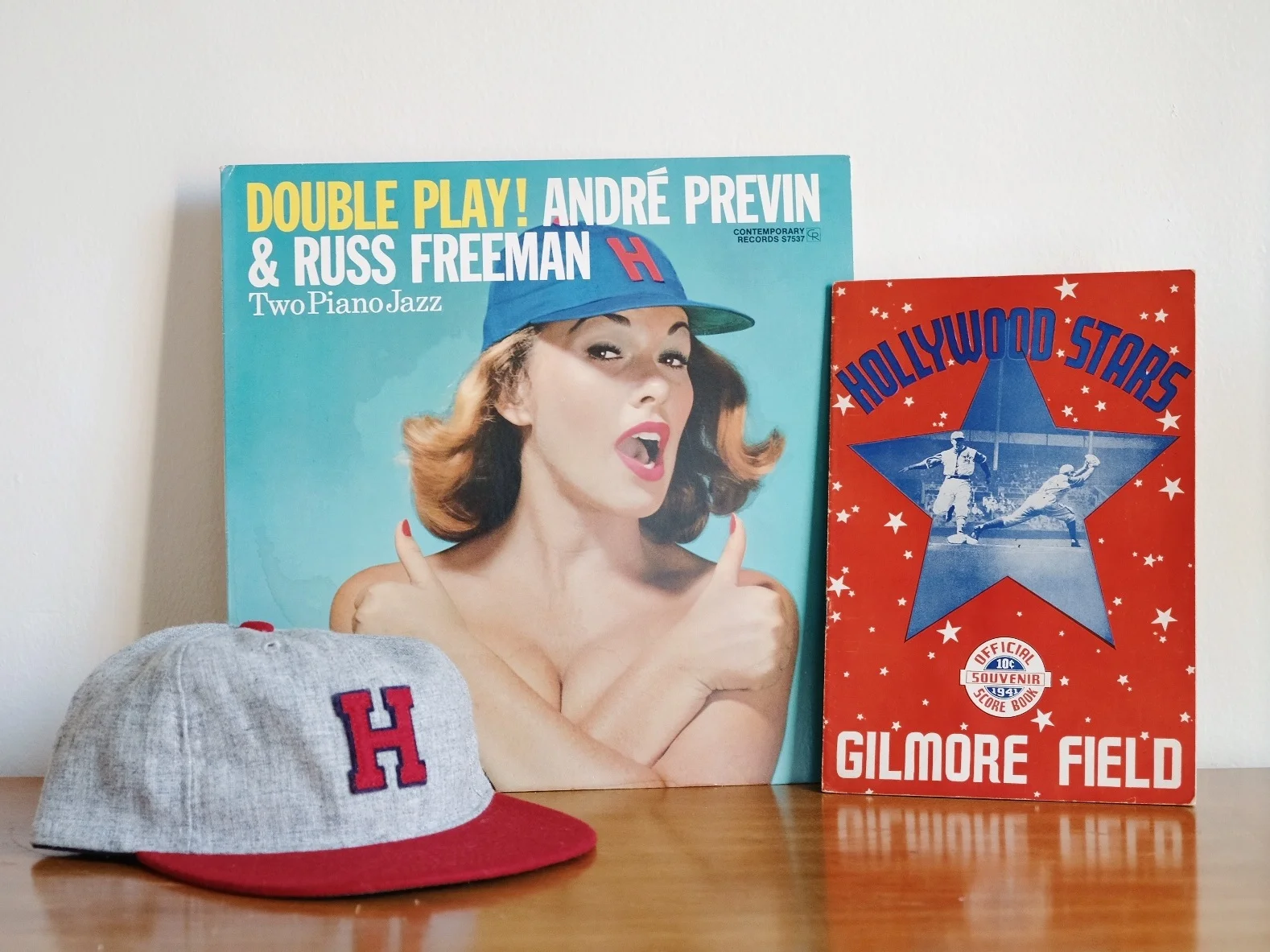 From the FLA Archives (from left): a reproduction Hollywood Stars hat from Ebbets Field Flannels , jazz album “Double Play!” (1957) featuring cover model wearing only a Hollywood Stars hat, and an official program from Gilmore Field (1941).