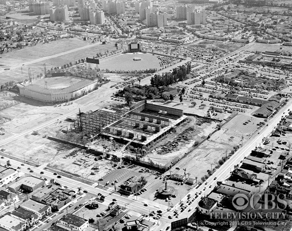 View of construction of CBS Television City looking southeast from Beverly and Fairfax, with Gilmore Field and the Gilmore drive-in in the background.