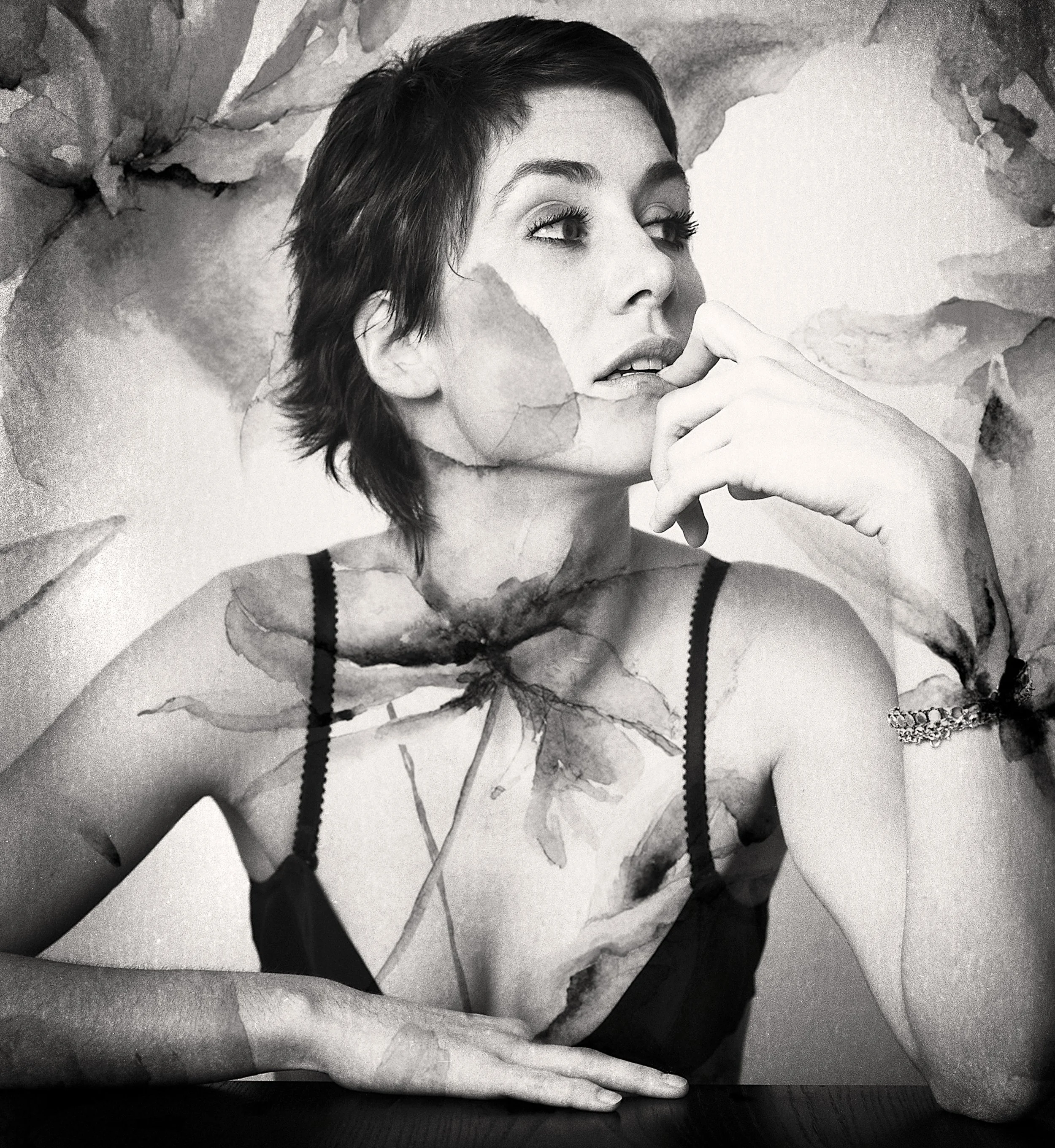 Une jeune femme en noir et blanc, avec une expression pensive, portant un pull noir avec des bretelles, se trouve devant un fond artistique abstrait.