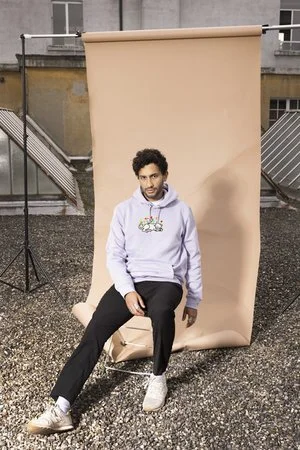 Jeune homme assis devant un fond beige sur un rooftop urbain.