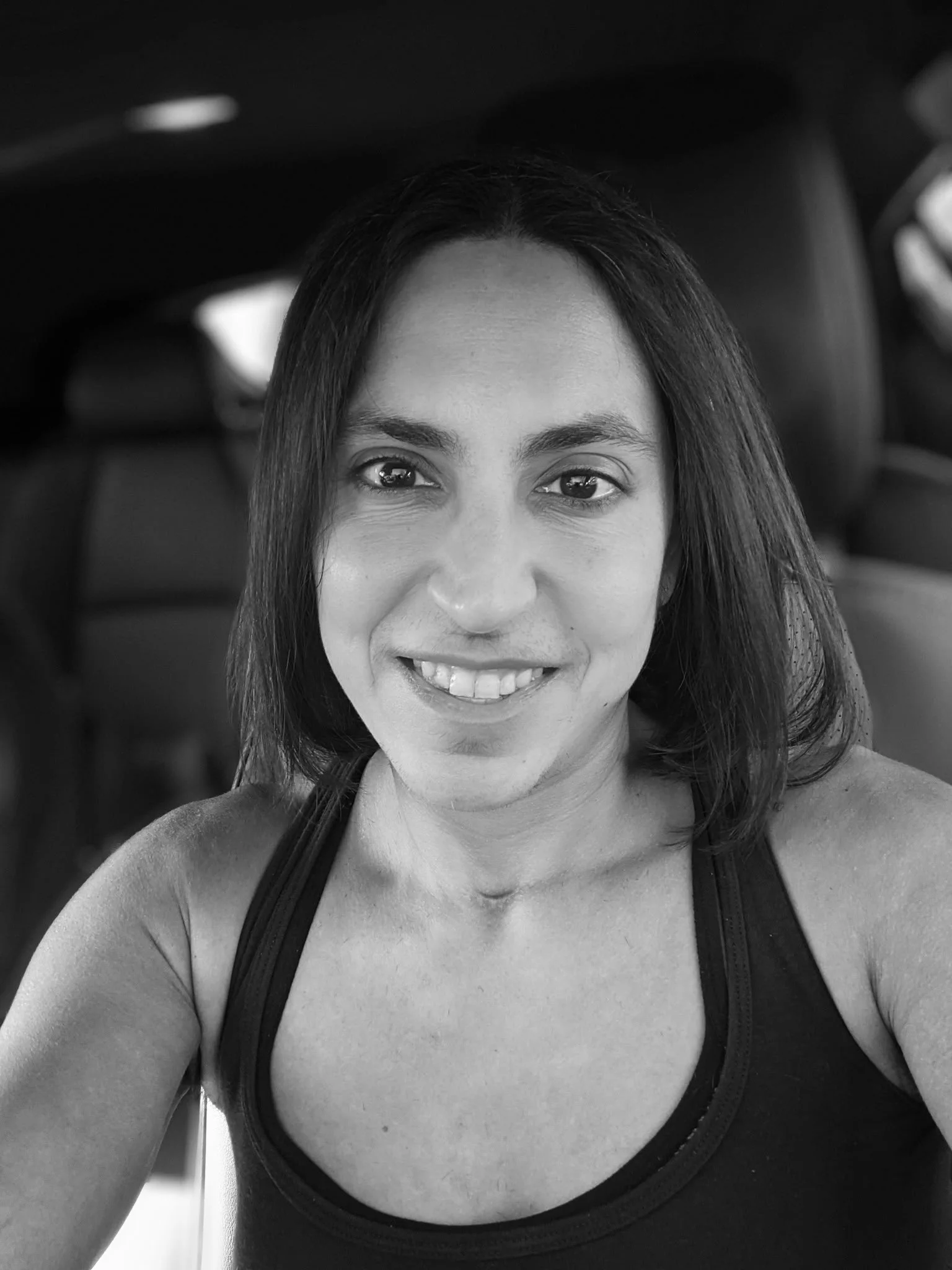 A woman with dark, hair taking a selfie in her car, in black and white.