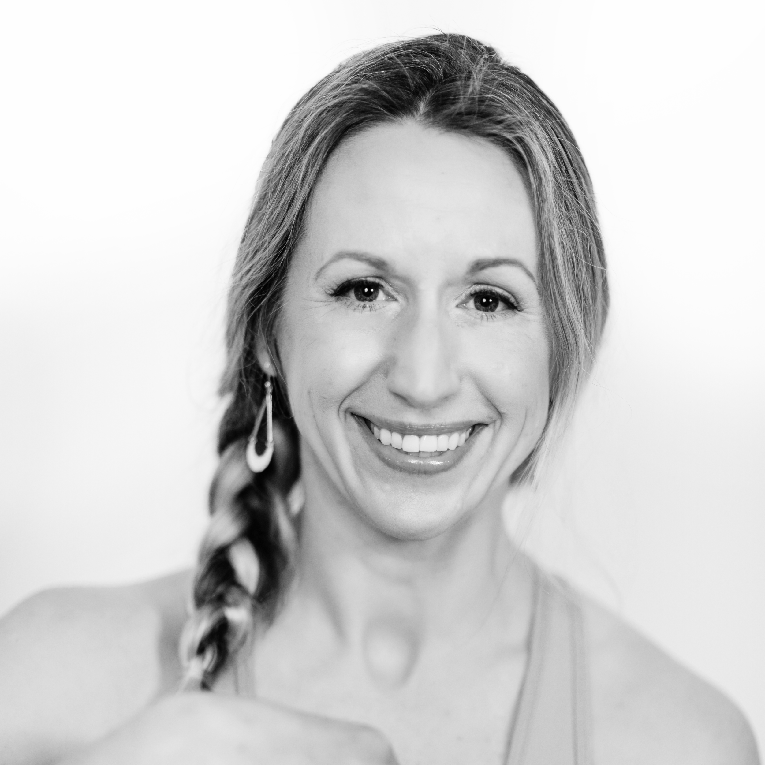 Black and white portrait of a woman smiling, with long braided hair, wearing earrings, and a tank top.