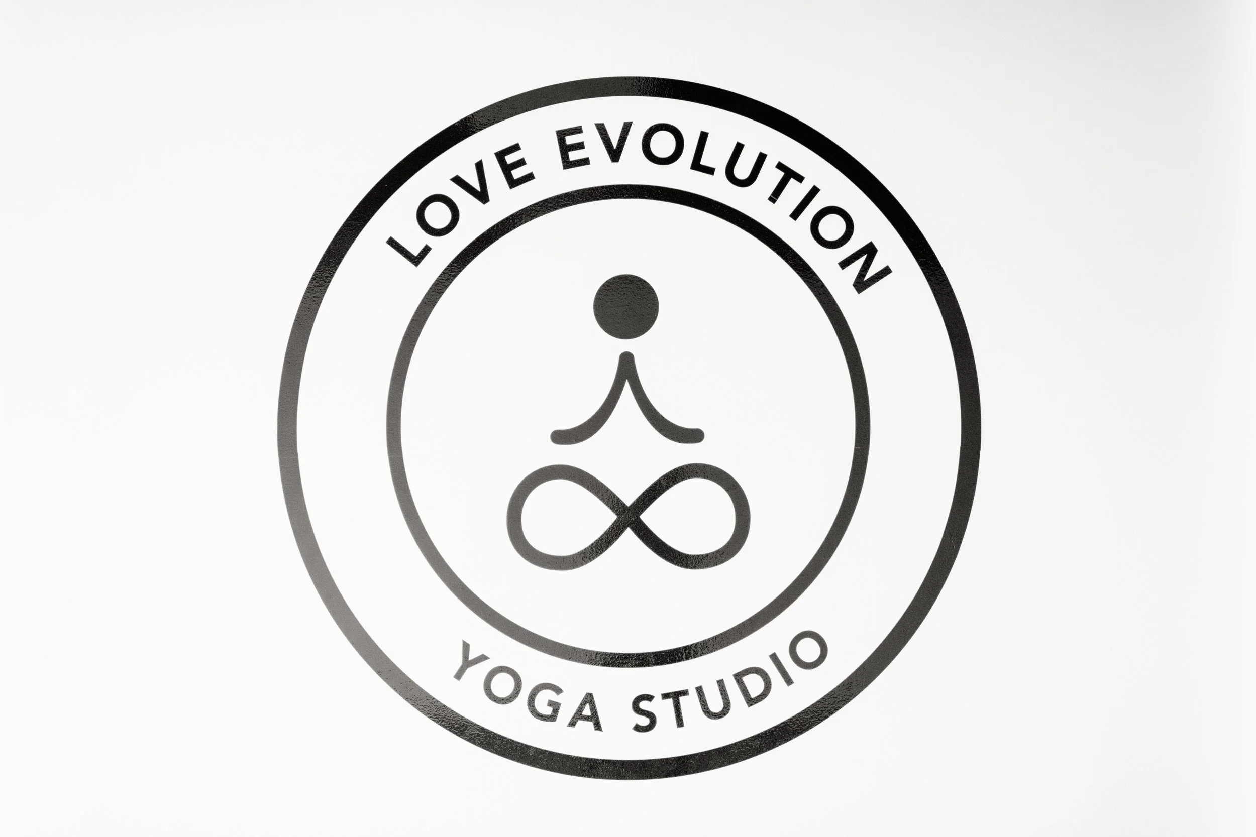 Logo for Love Evolution Yoga Studio featuring a stylized person in a yoga pose with an infinity symbol for legs, surrounded by the text 'LOVE EVOLUTION YOGA STUDIO'.