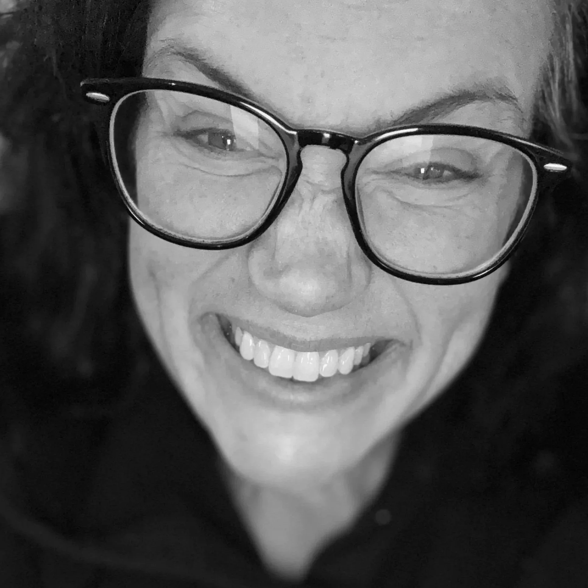 A woman with glasses smiling in black and white.