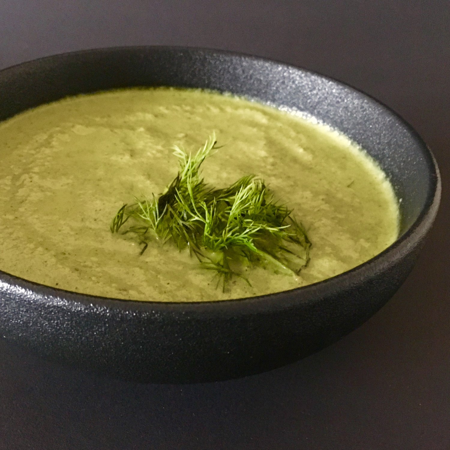 A pot of cauliflower leaf soup simmers on a stove, surrounded by colorful vegetables and herbs. A cookbook titled "30 Sustainable Recipes That Reduce Food Waste" sits open nearby