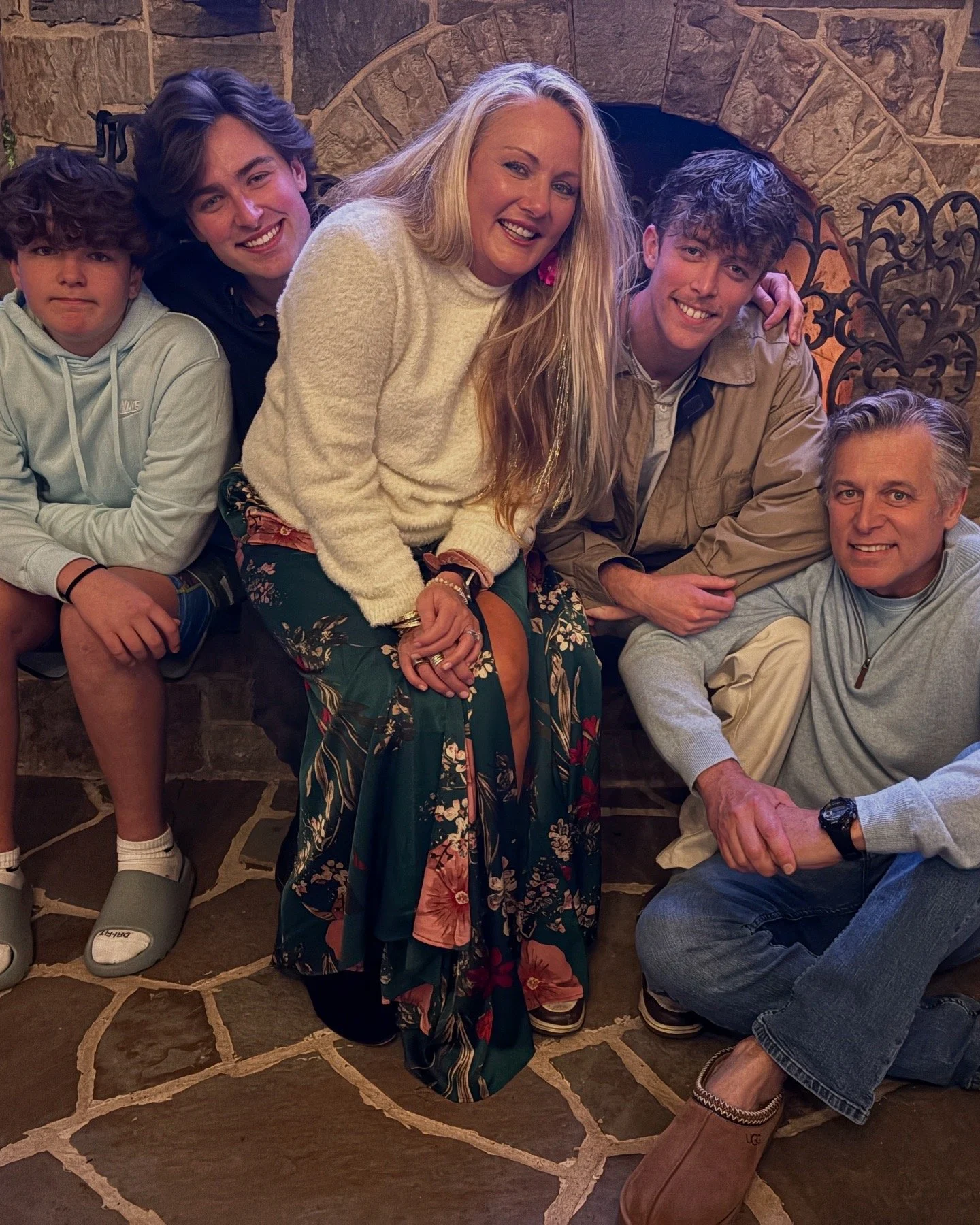 Group of five people, three men and two women, gathered around a fireplace, smiling and posing for the camera.