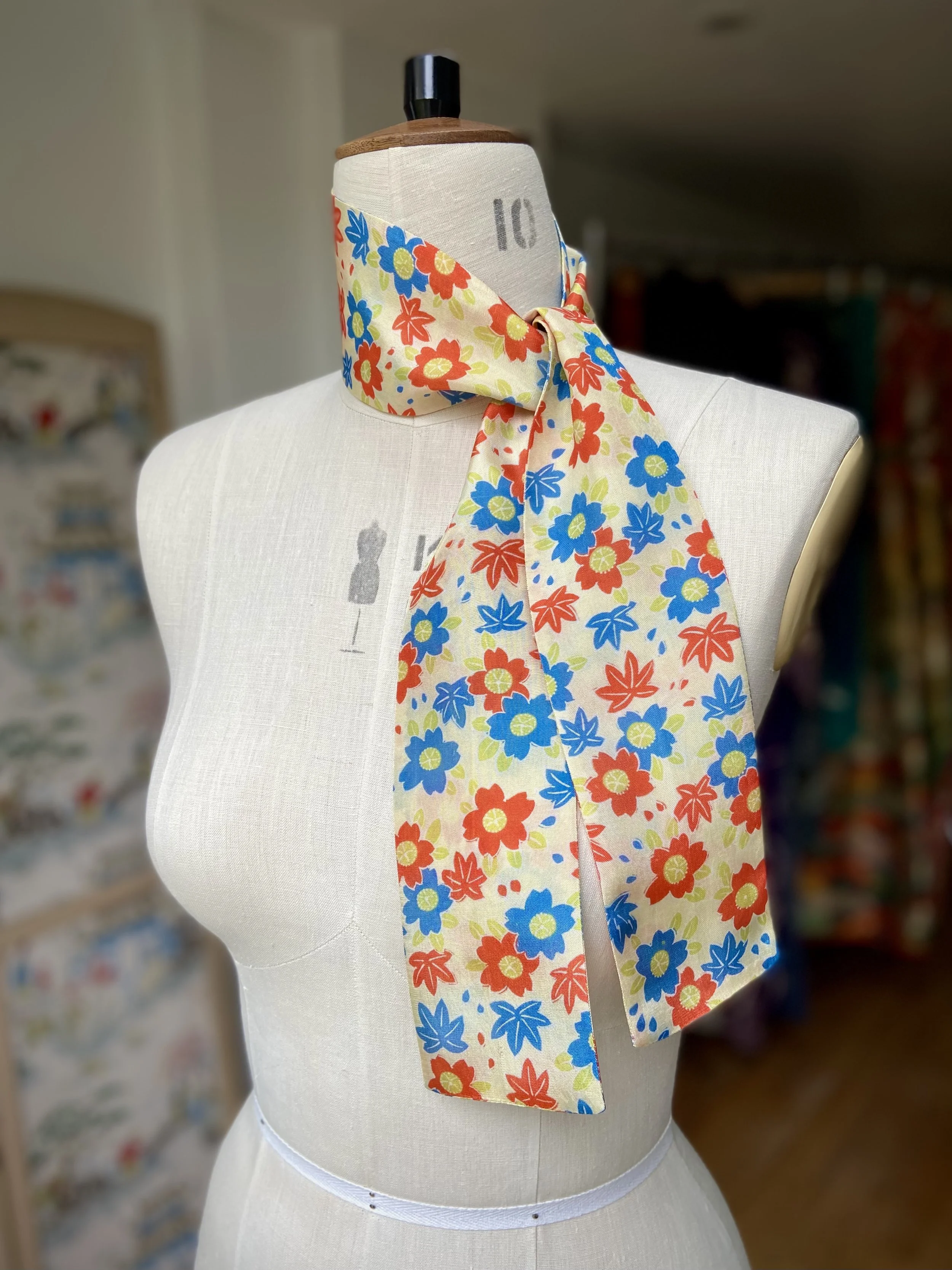 Pale yellow skinny scarf presented on a dress stand, with printed cherry blossom design, handmade from repurposed kimono fabric by Kirsty Chivers