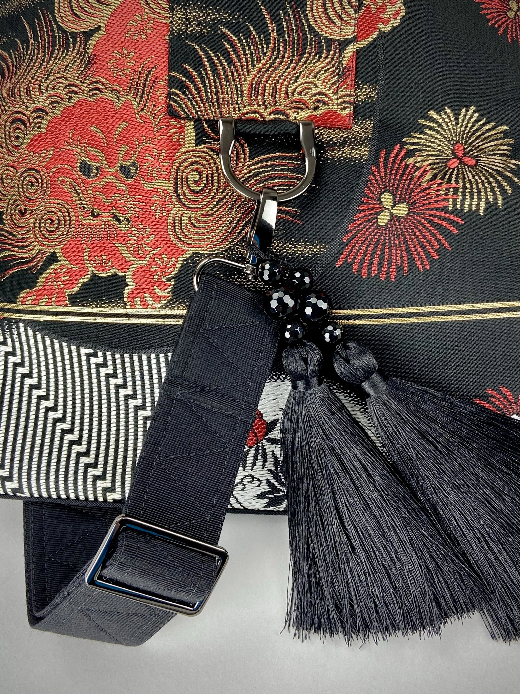 Closeup of black matt satin silk and rayon obi bag with red, green, gold and ivory dragon motifs, gunmetal hardware and black tassel charm by Kirsty Chivers